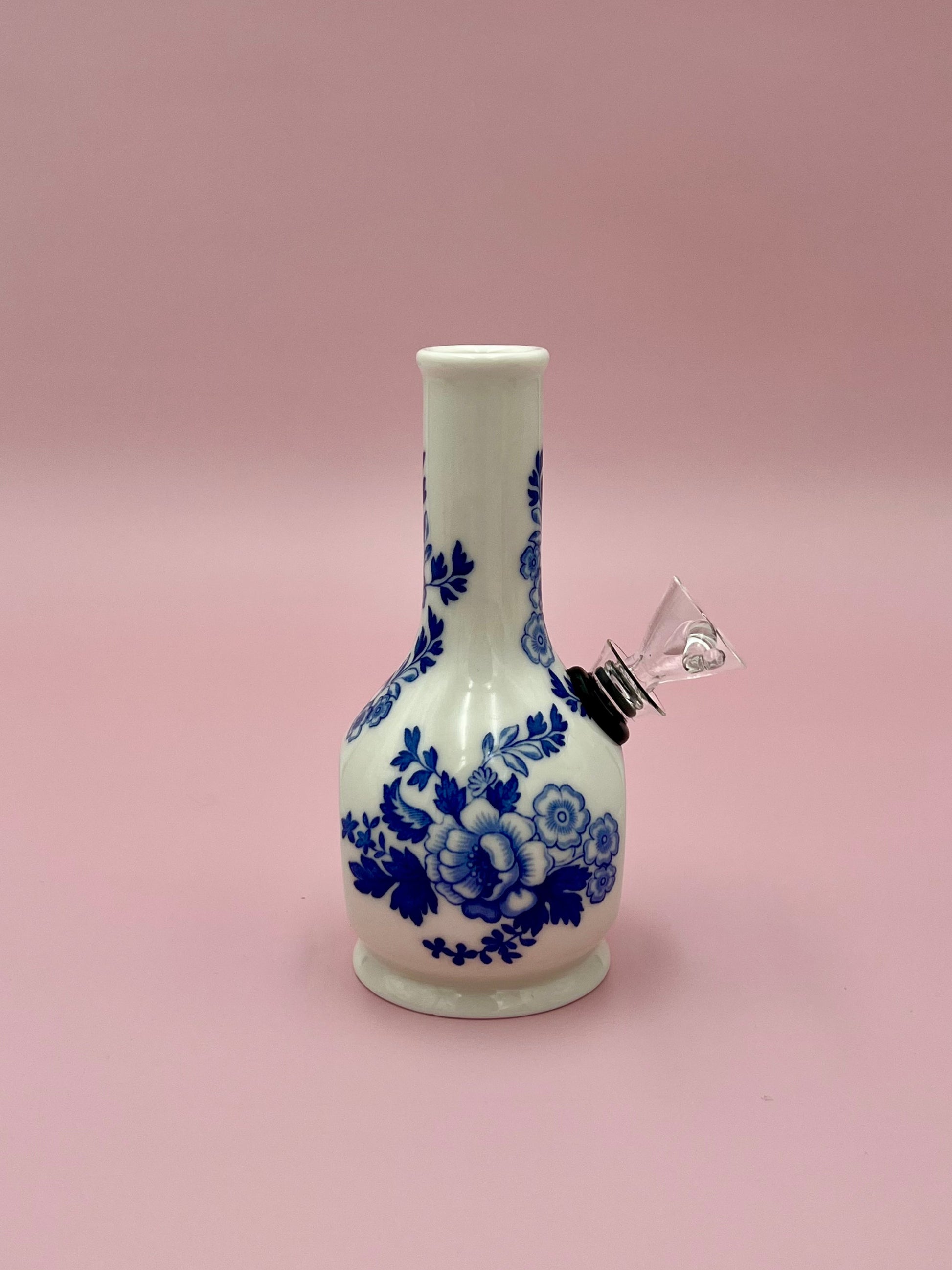 Angled view of the Betty water pipe showing the glass fittings and blue floral pattern along the neck, pink background.