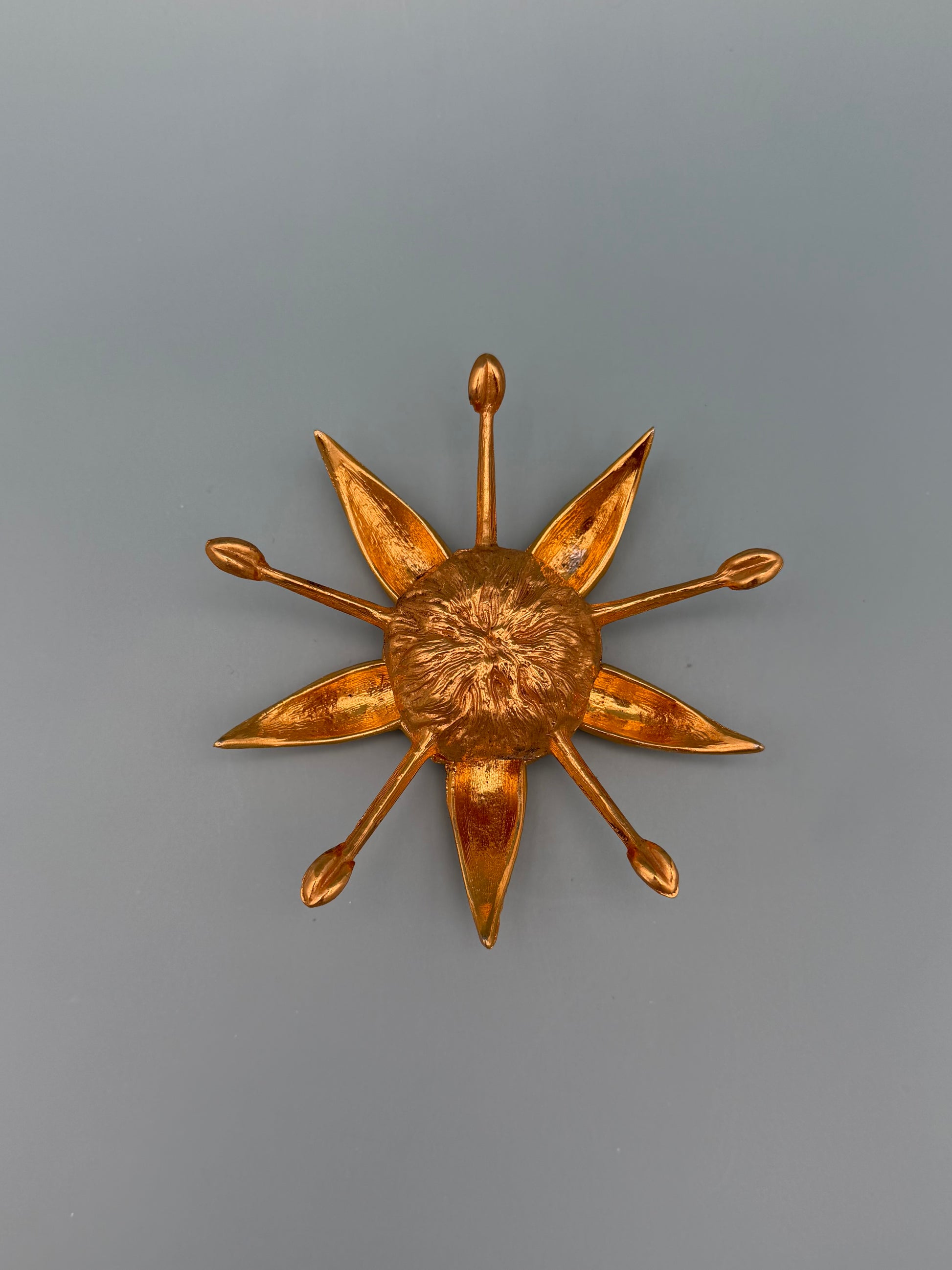 Gold starburst-shaped dish with pointed rays radiating from a textured center, gray-blue background.