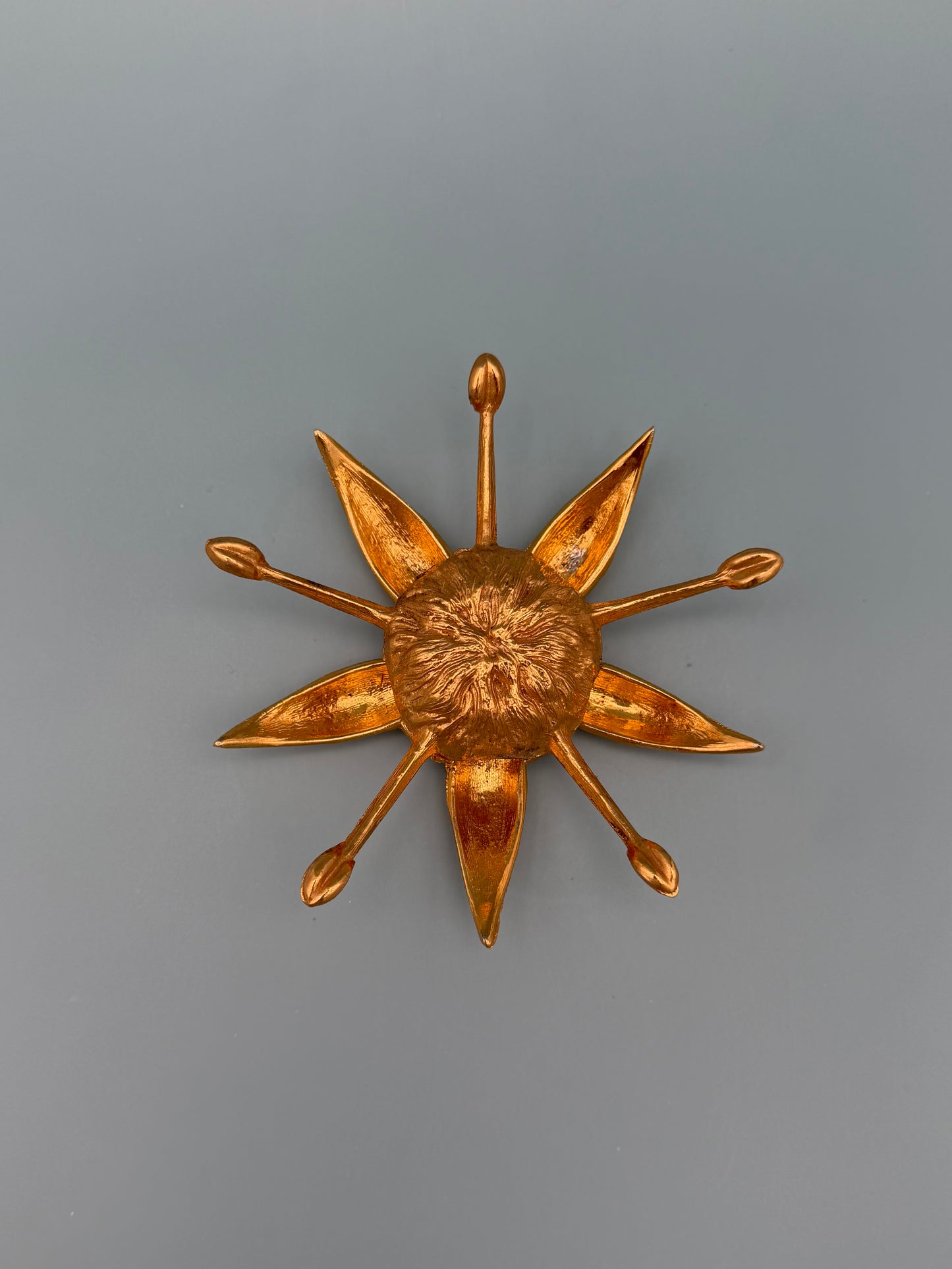 Gold starburst-shaped dish with pointed rays radiating from a textured center, gray-blue background.