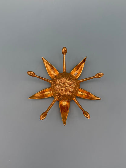 Gold starburst-shaped dish with pointed rays radiating from a textured center, gray-blue background.