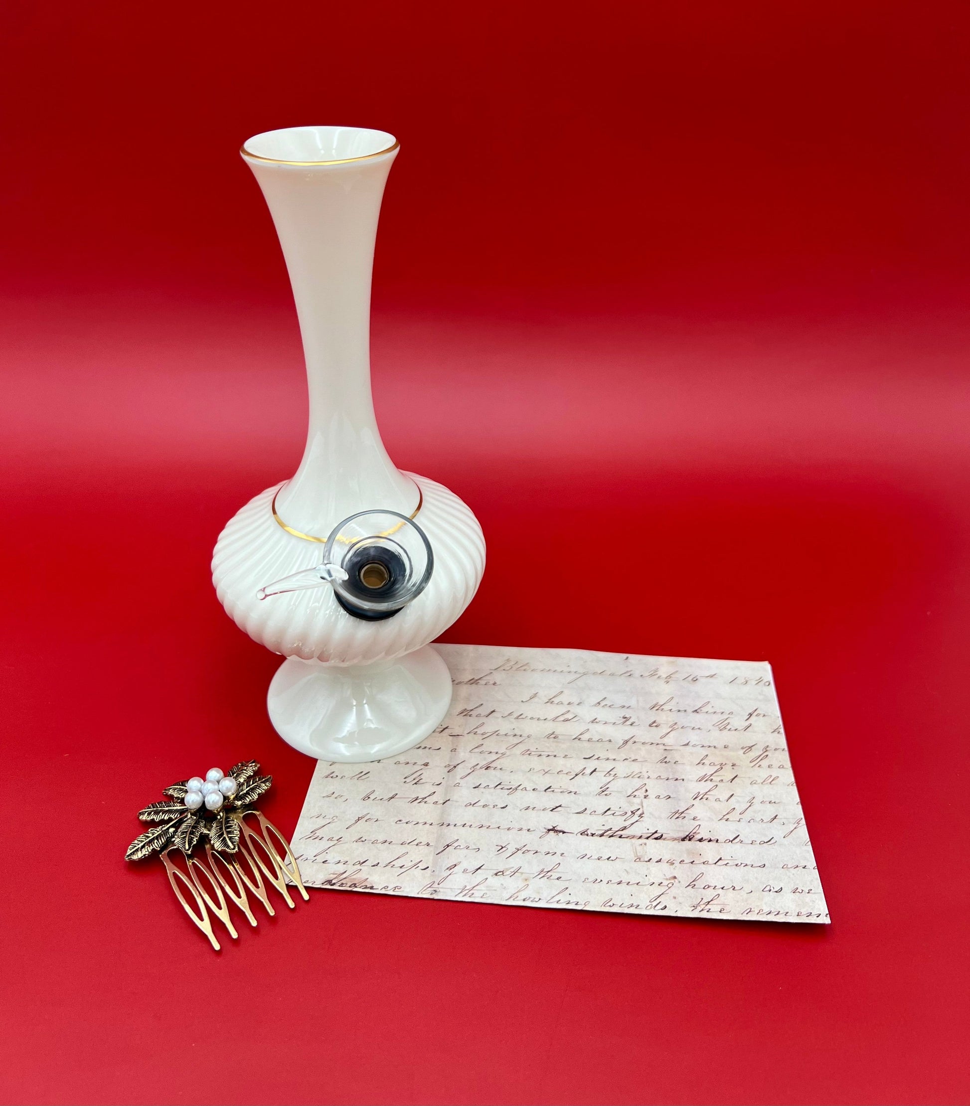 Carol water pipe styled with a vintage handwritten letter and a small jeweled hair comb, deep red background.