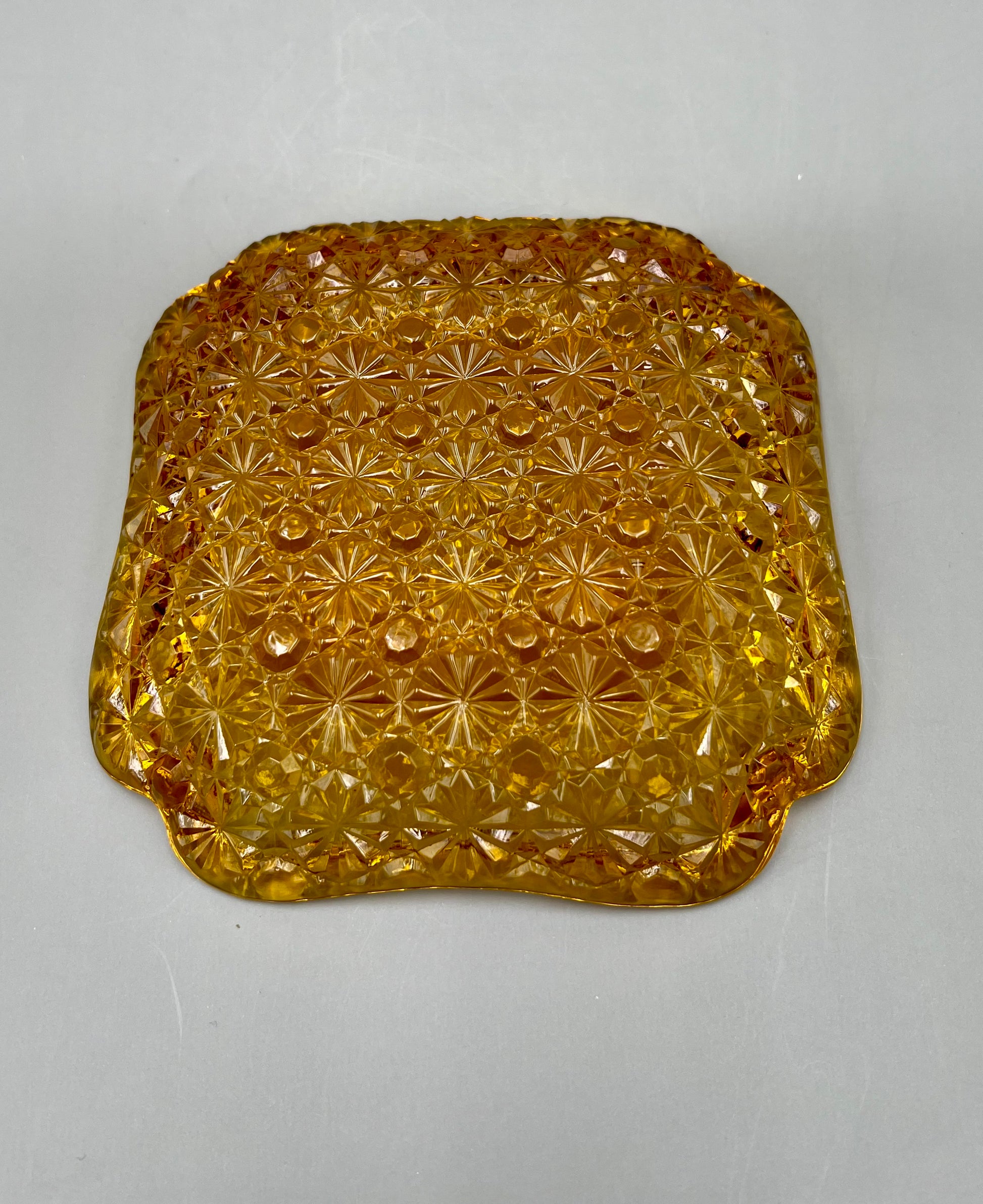 Amber pressed-glass daisy and button ashtray shown from a top-down angle, gray background