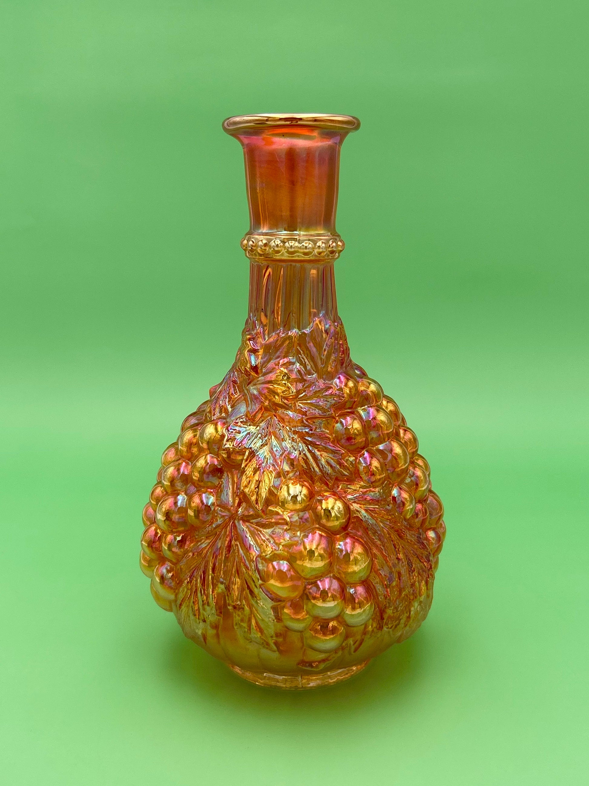 Same marigold iridescent carnival glass decanter, plain front view with no attachment visible, green background