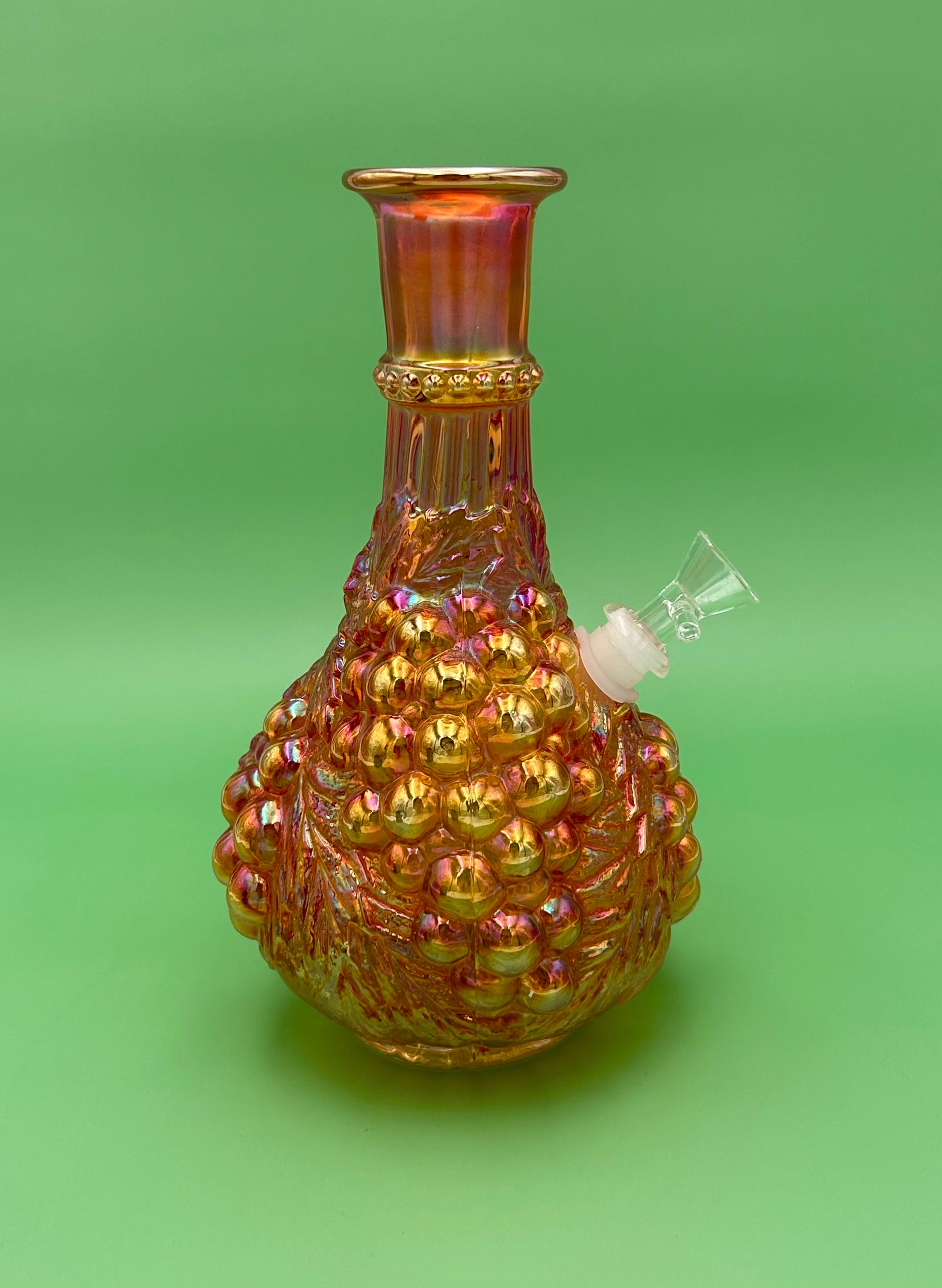 Same marigold iridescent carnival glass decanter, clear glass mouthpiece attached at the side, viewed from a different angle, green background