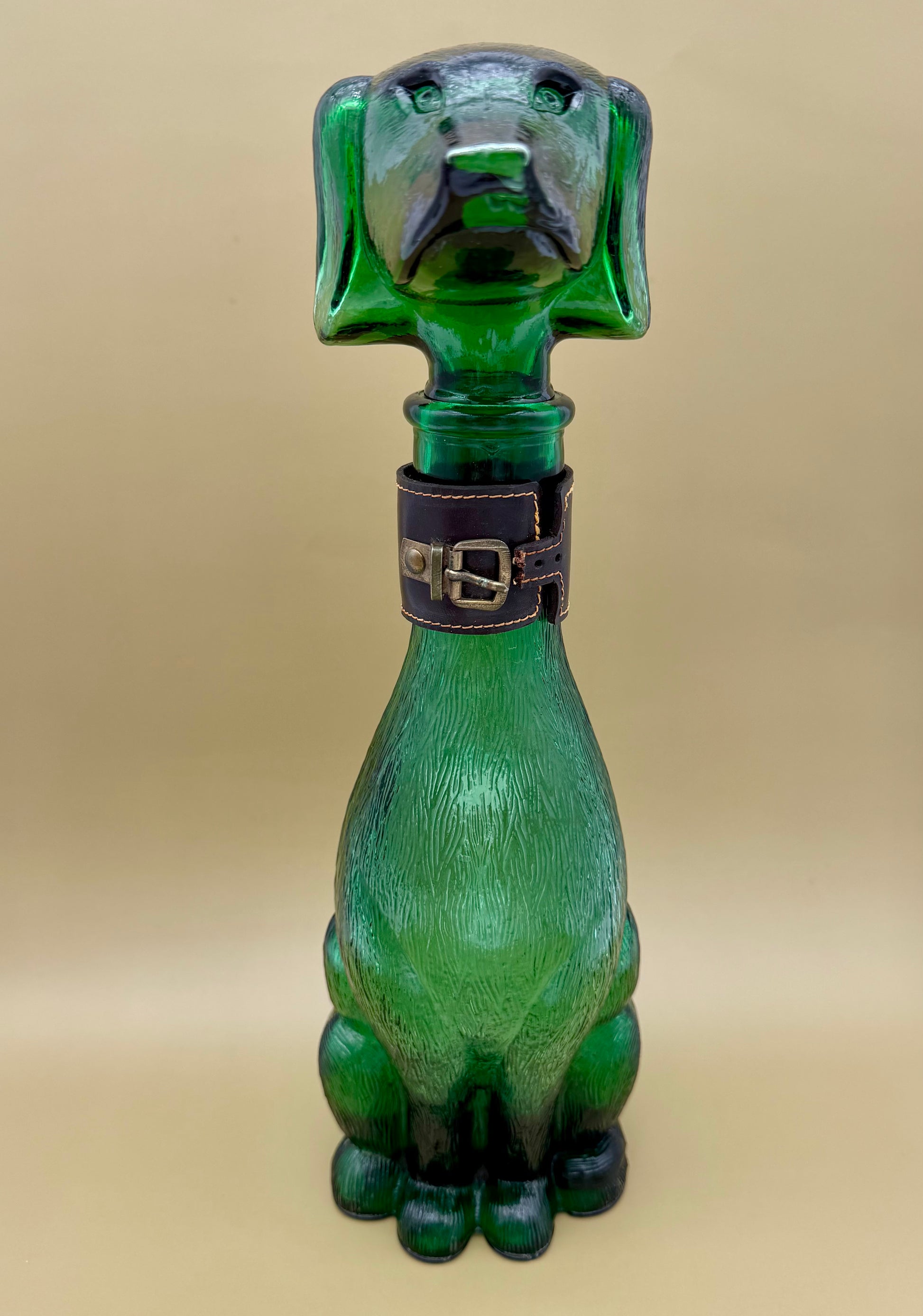 Front view of the green glass dachshund-shaped decanter water pipe showing its face and studded collar, tan background.