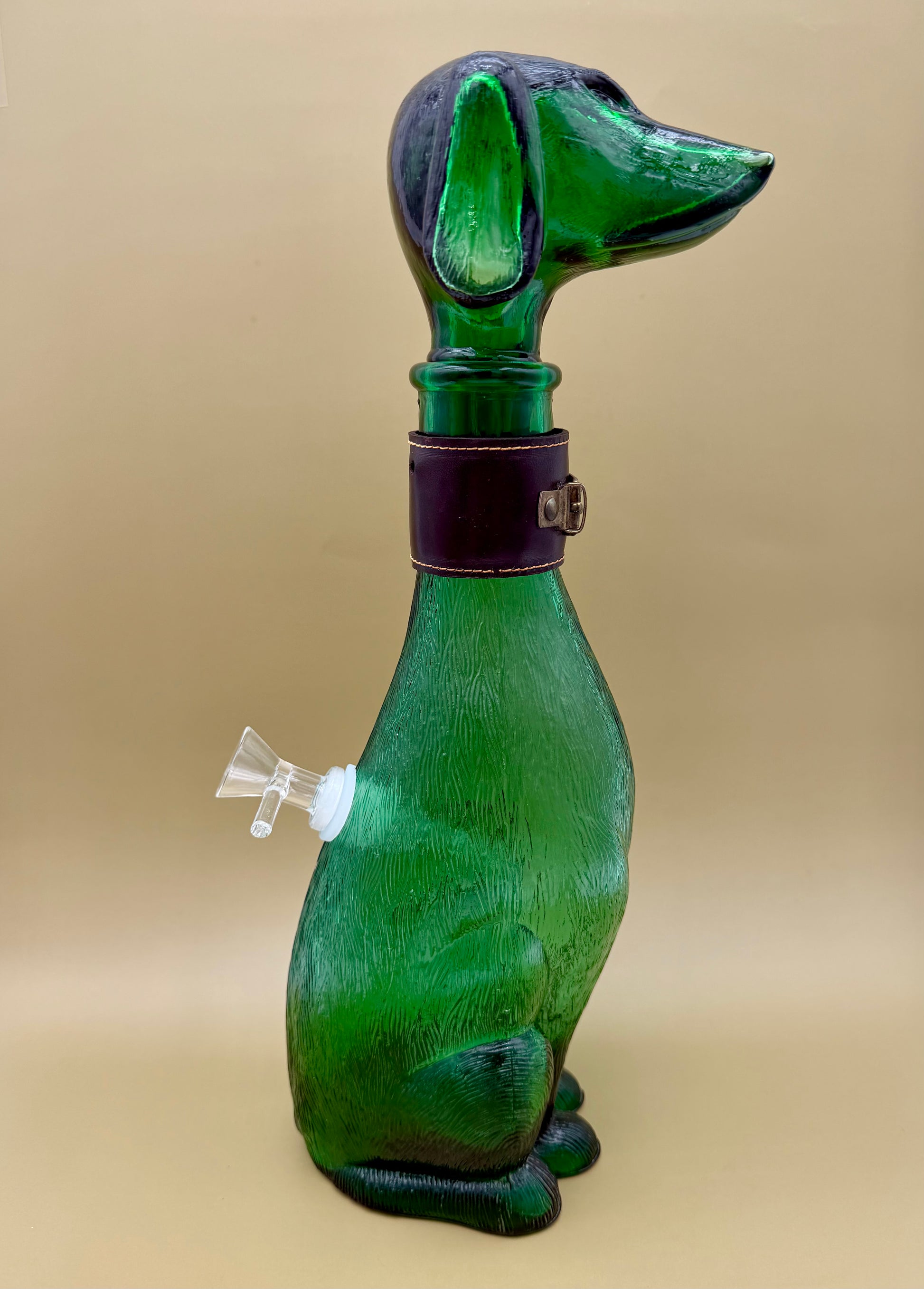 Three-quarter rear view of the green glass dog decanter showing the glass bowl piece attached at its side, tan background.