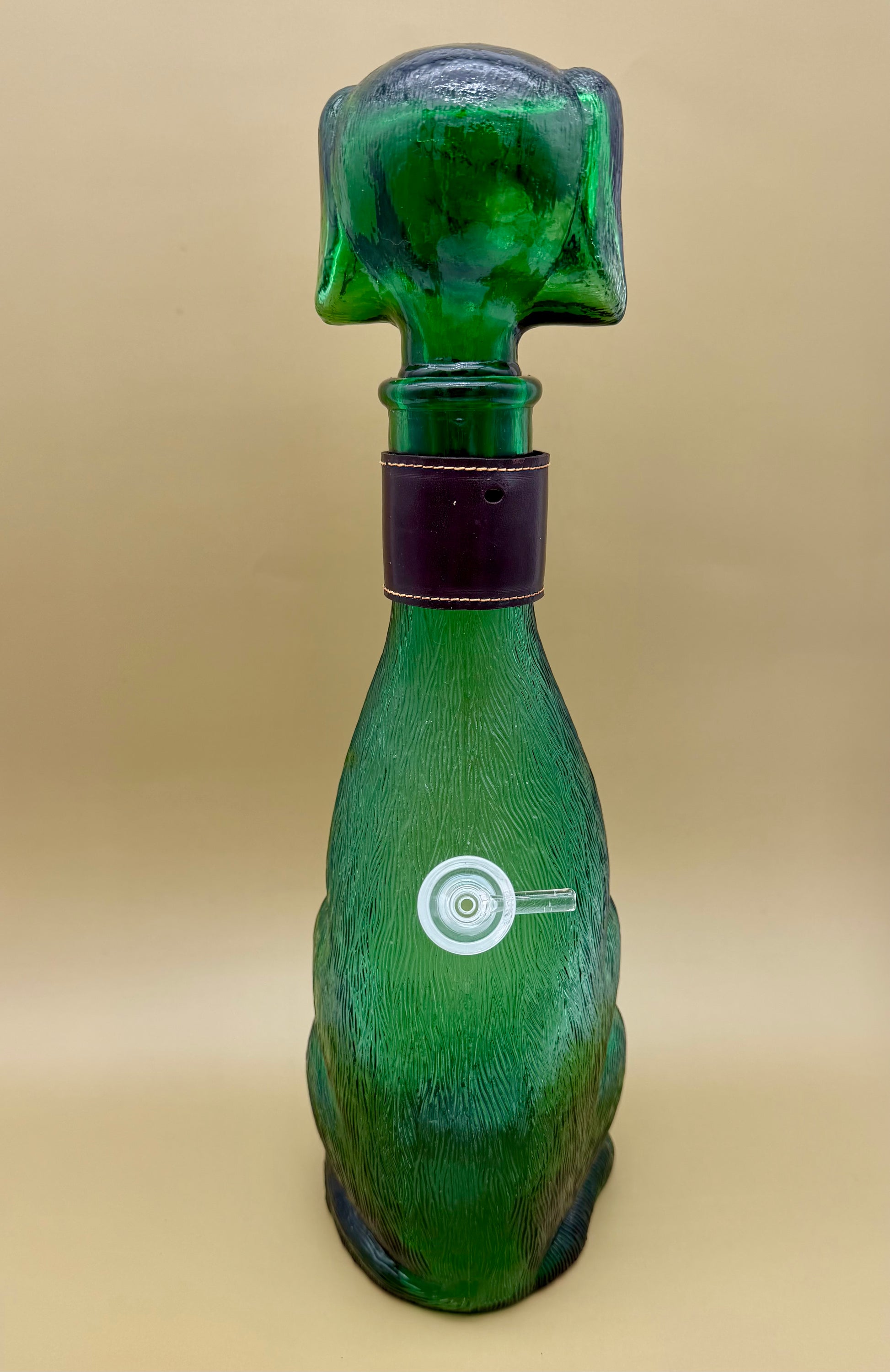 Front view of the green glass dog decanter showing a round glass carb piece at its belly, tan background.