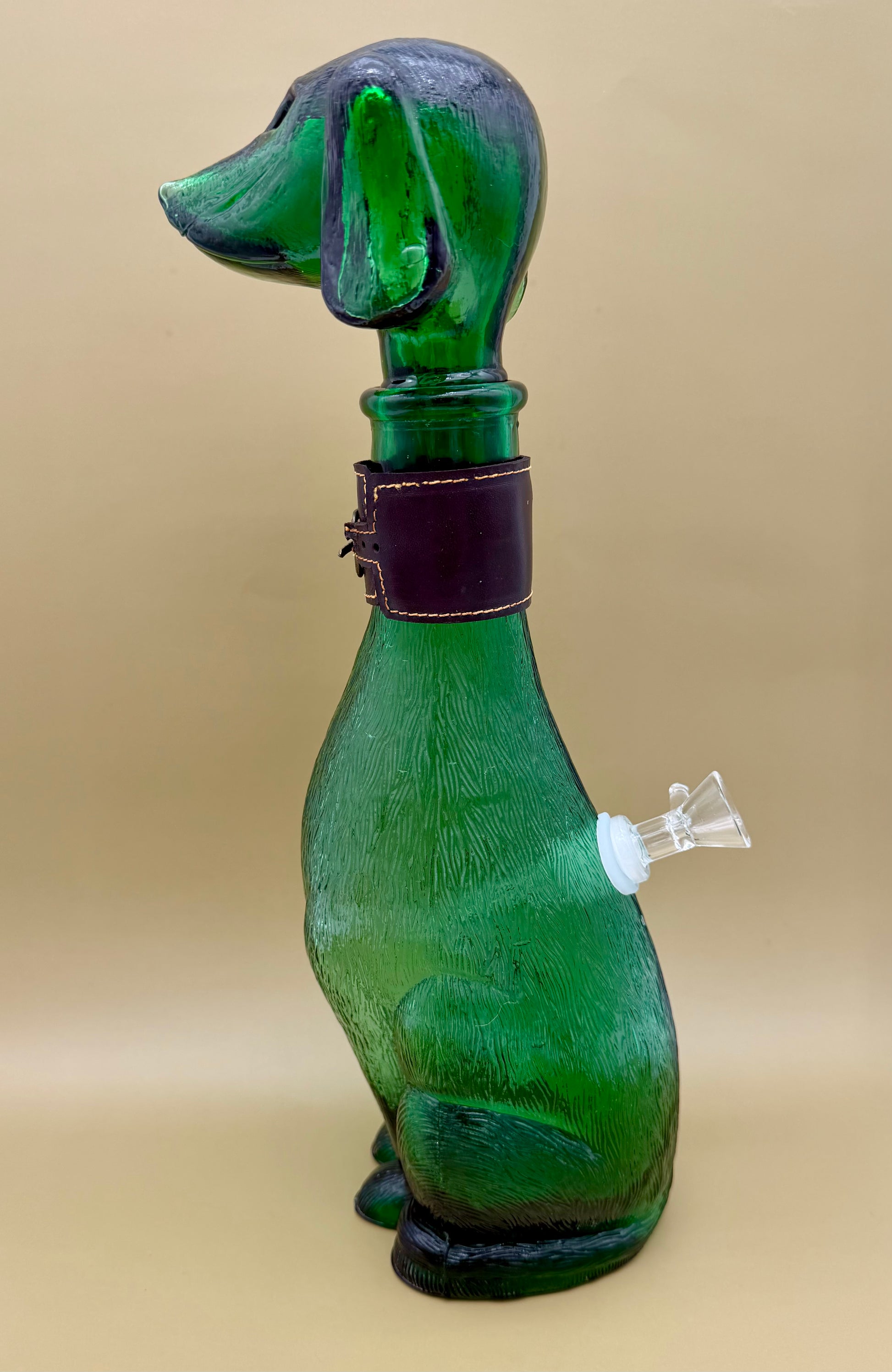 Side profile of the green glass dog decanter showing the glass bowl piece attached at the side, tan background.