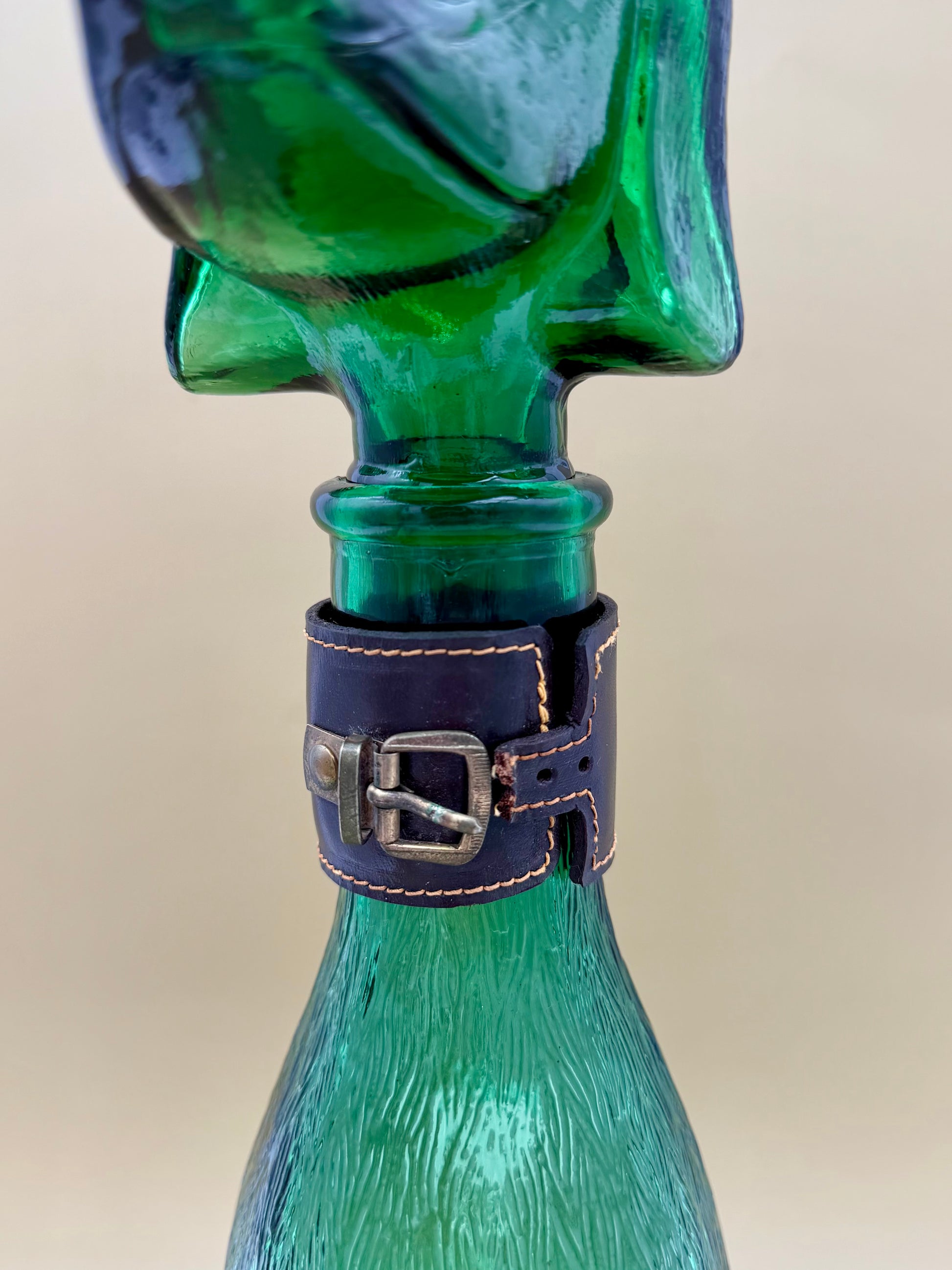 Close-up of the green glass dog decanter's neck showing the removable ear-shaped stopper and studded collar detail, tan background.