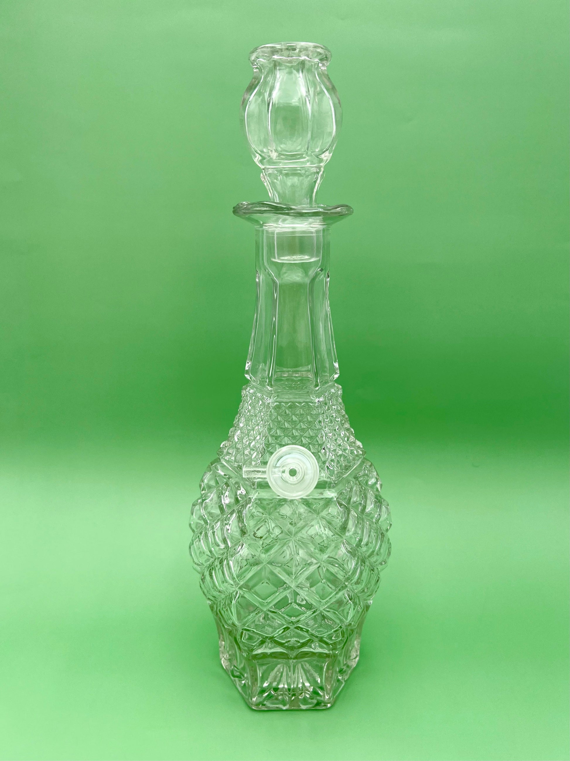 Front view of a clear cut-glass decanter water pipe with a faceted diamond pattern and glass stopper, green background.