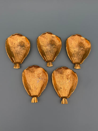 Five gold teardrop-shaped petal dishes scattered separately, gray-blue background.