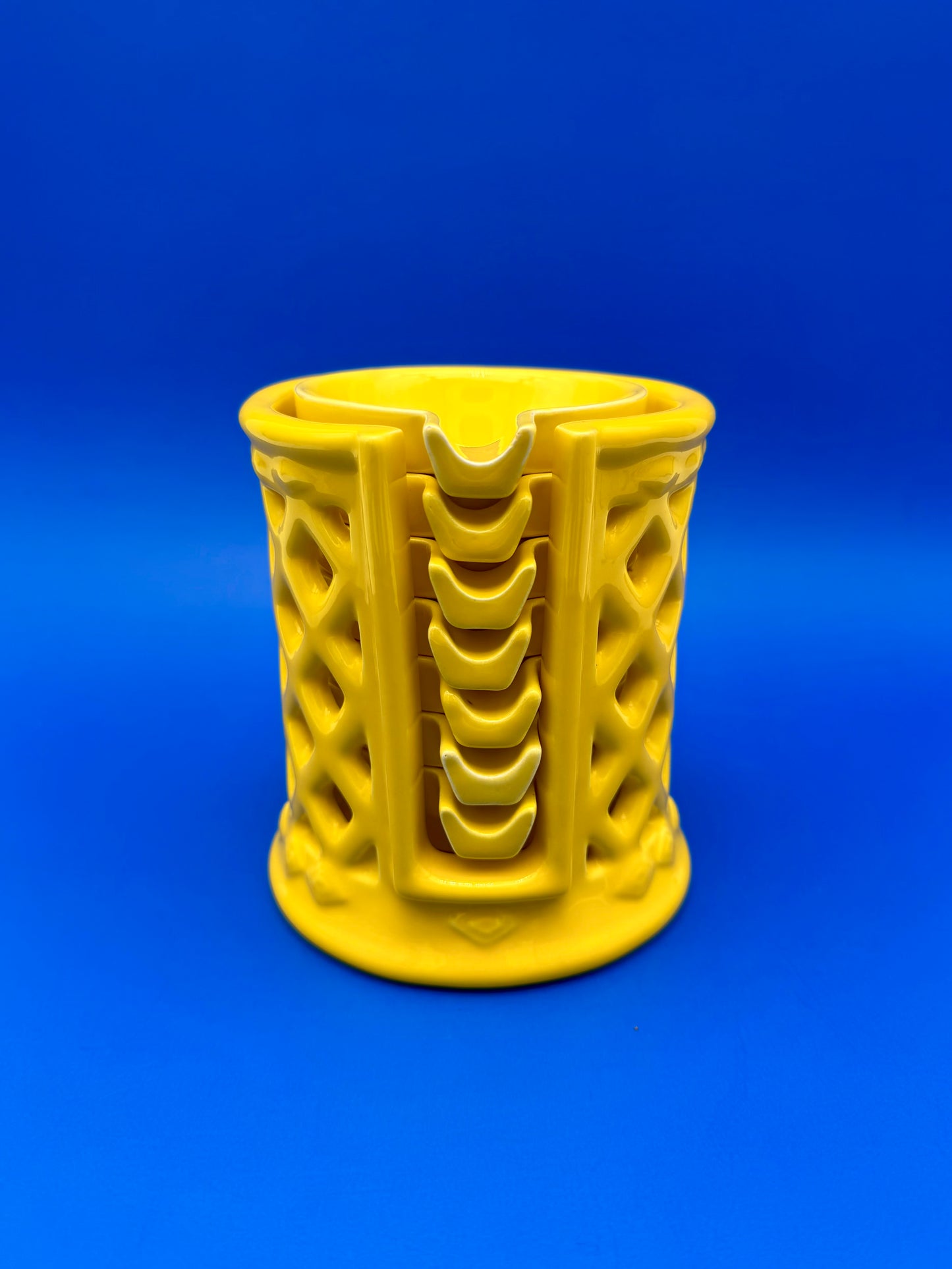 Yellow ceramic lattice-cut ashtray holder alone with vertical ribbed design, blue background