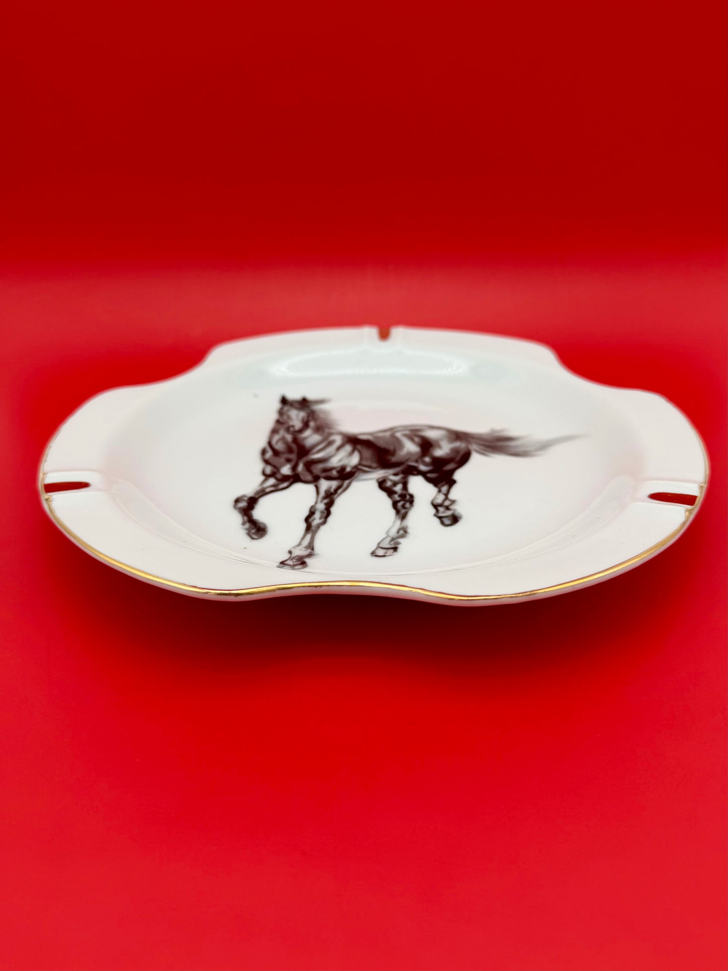 White scalloped ashtray from Duke showing a full-body illustration of a galloping horse, shown without the cigarette pick, red background.