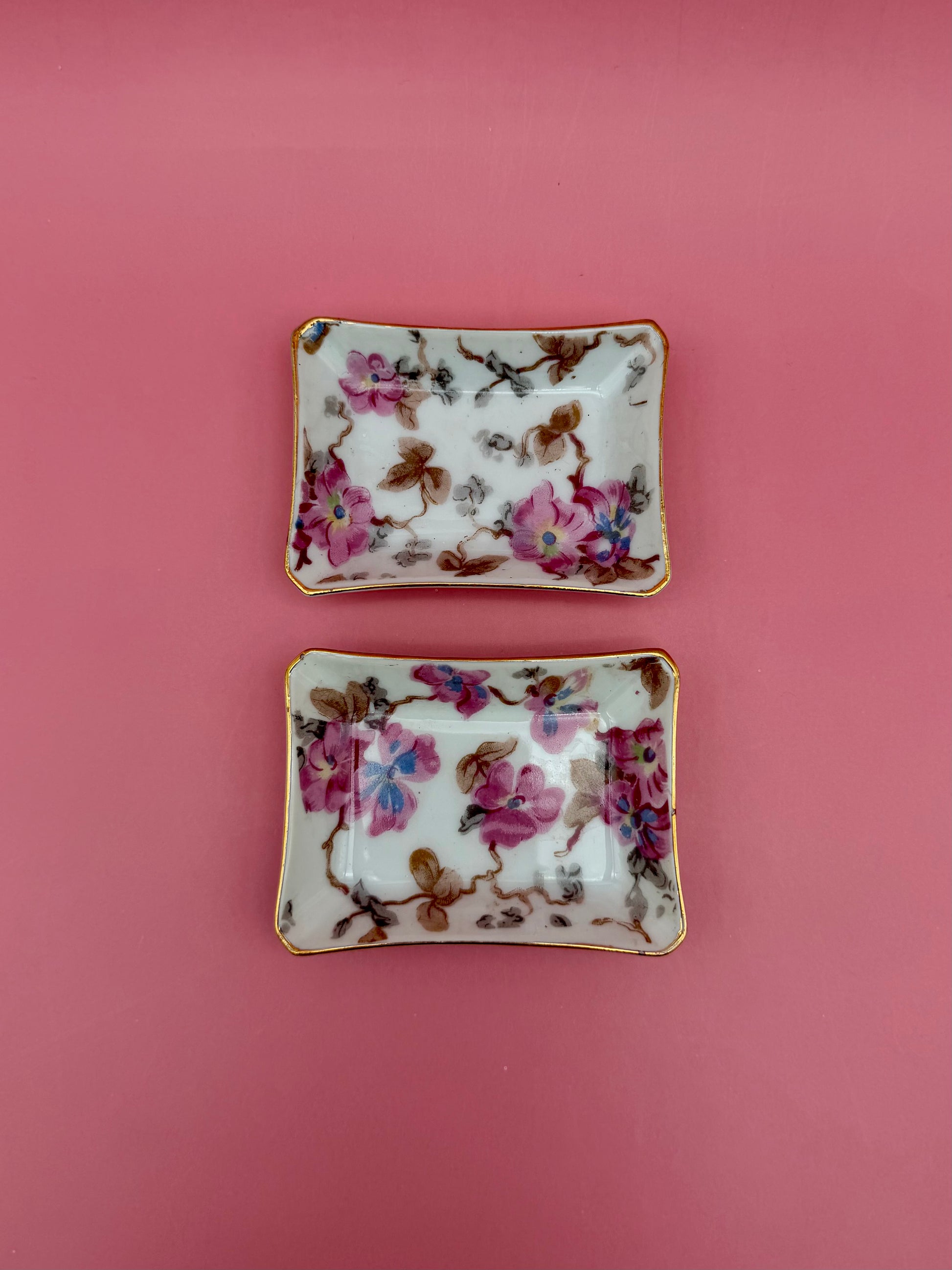 Two floral porcelain ashtrays with pastel flower and leaf design side by side, pink background