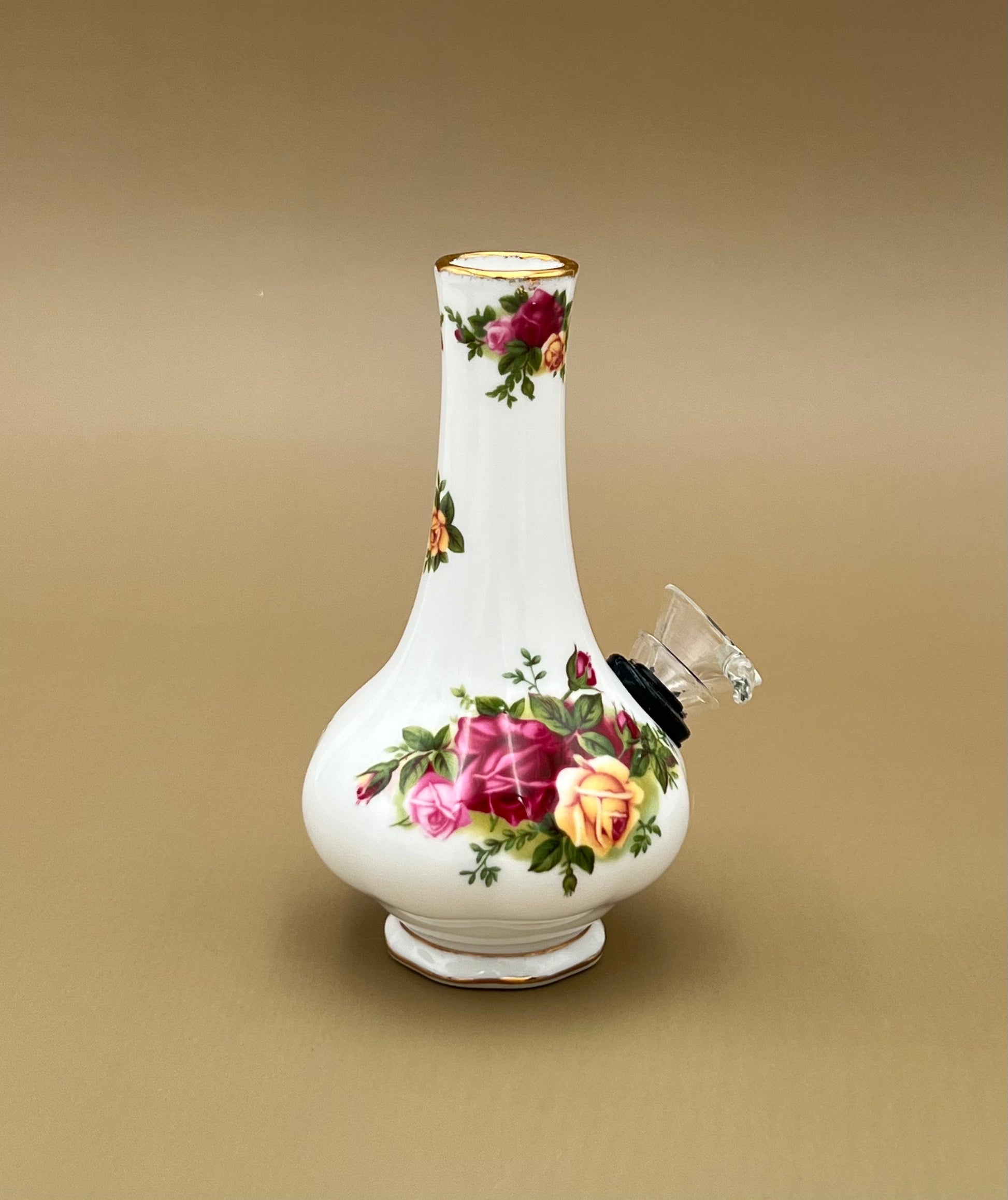 Angled view of the same white porcelain bud vase water pipe with its painted rose bouquet and gold trim, gray-tan background.