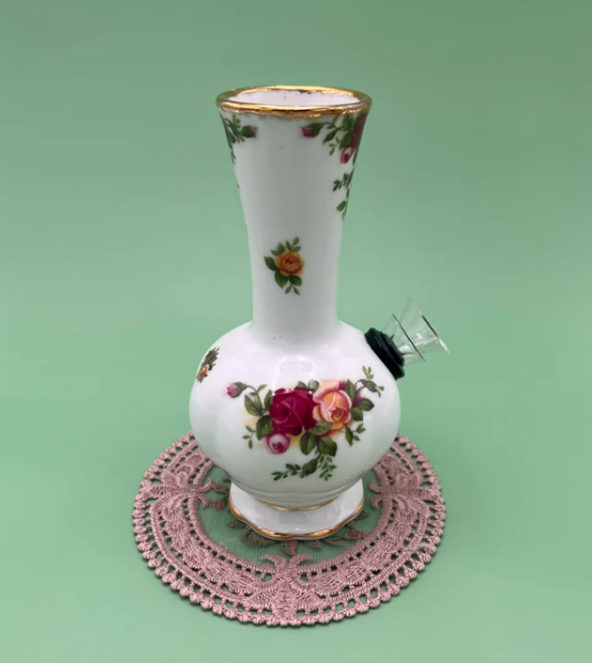 White fine bone china bud vase water pipe with hand-painted burgundy, pink, and yellow rose bouquet and gold rim, glass bowl piece attached at the side, displayed on a pink crocheted doily against a sage green backdrop.
