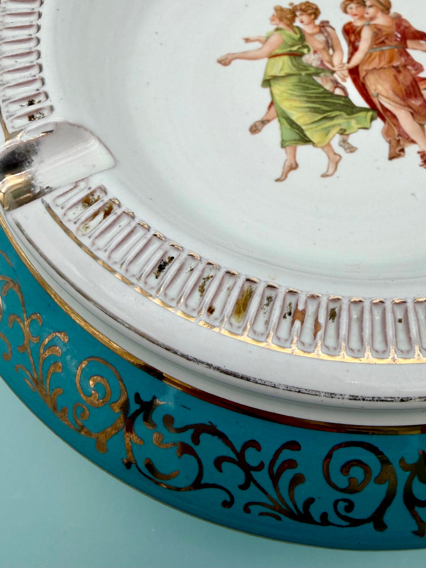 Close-up of the dancing figures medallion with ornate gold scrollwork and turquoise porcelain rim