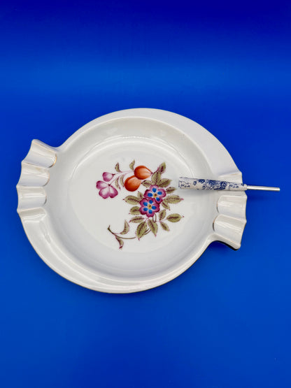 White porcelain ashtray with a colorful floral and berry center design and a cigarette pick, blue background