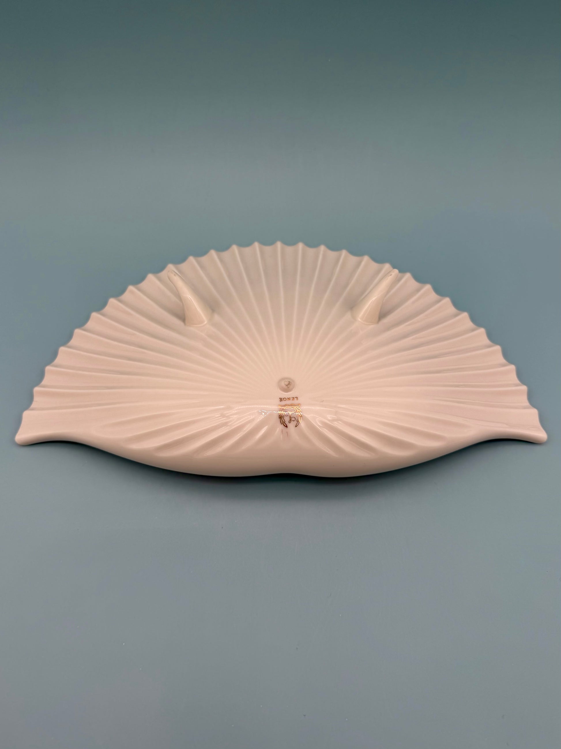 Cream and ivory toned seashell-shaped porcelain ashtray shown at an angle, gray background