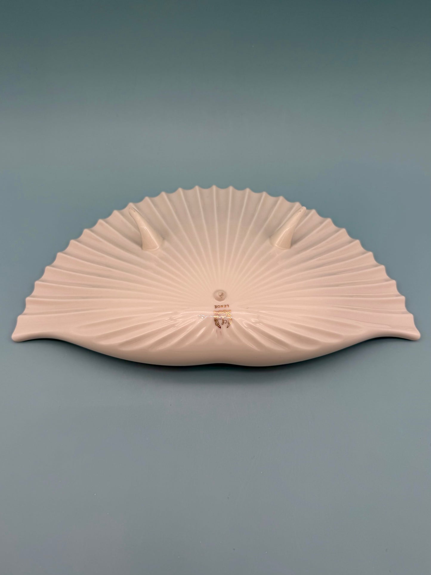 Cream and ivory toned seashell-shaped porcelain ashtray shown at an angle, gray background
