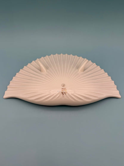 Cream and ivory toned seashell-shaped porcelain ashtray shown at an angle, gray background