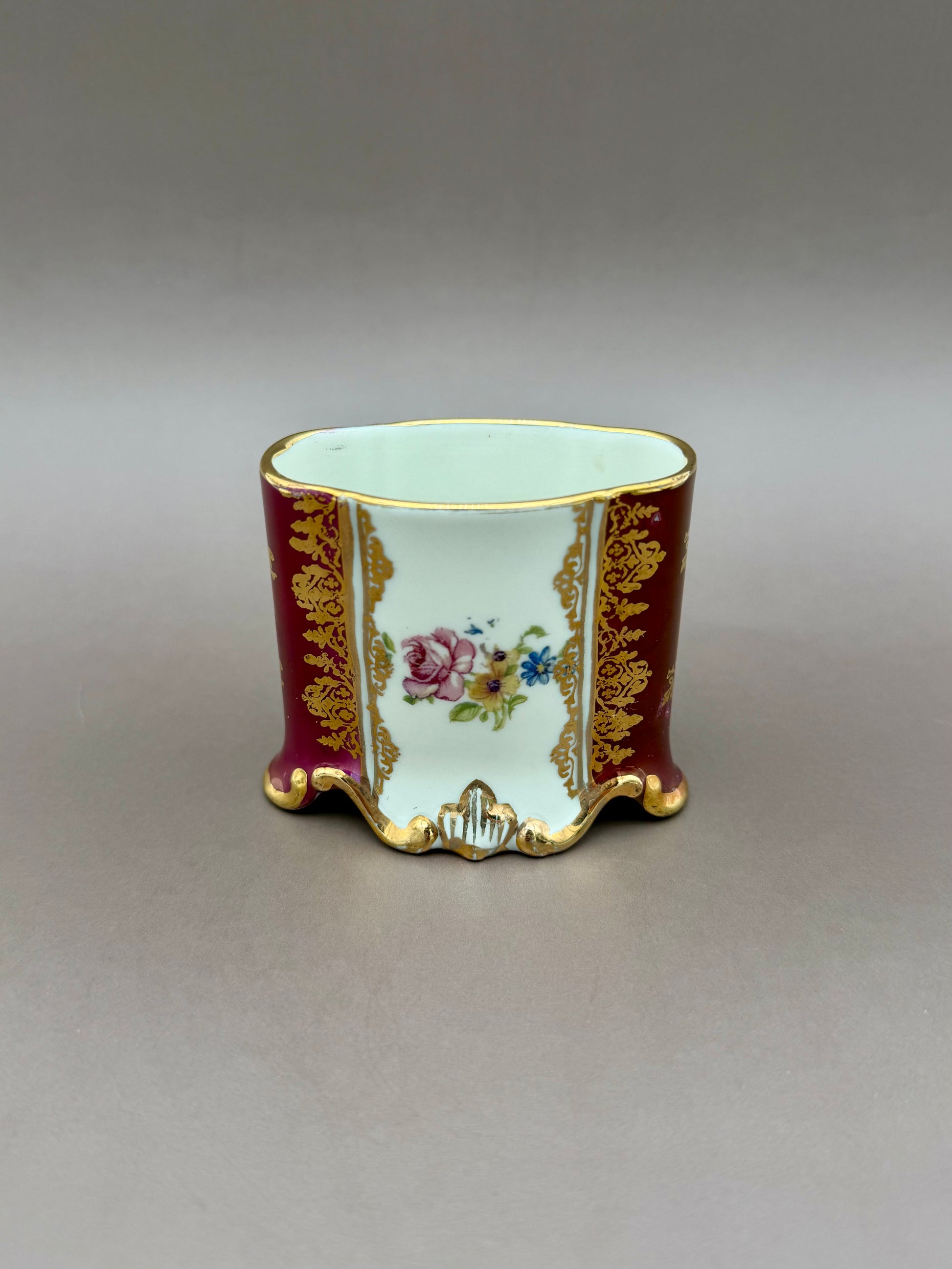 The Henrietta Set cup shown from another side, displaying a burgundy panel with a painted floral medallion instead of a portrait, gray background.