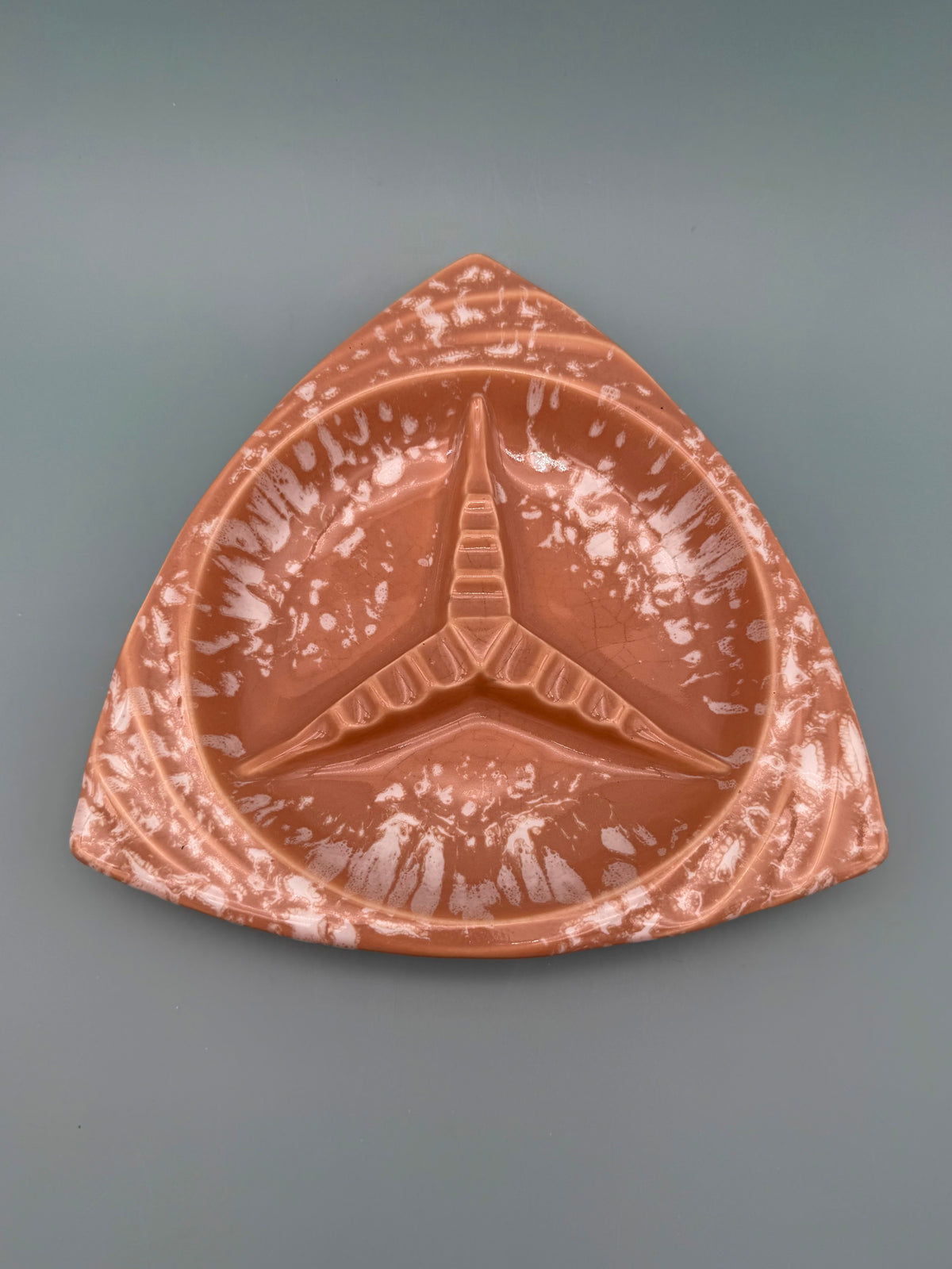 Triangular terracotta ceramic ashtray with a speckled glaze and three cigarette rests, gray background.