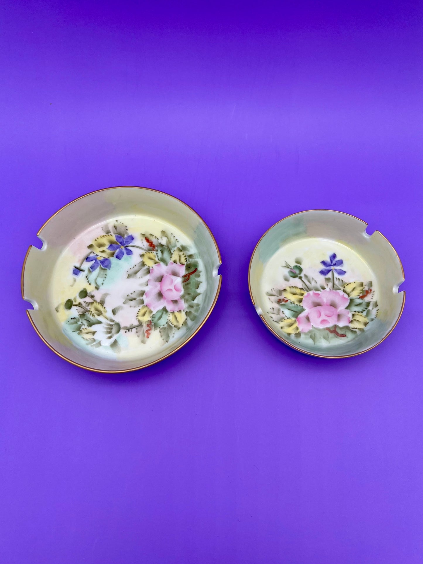 Katherine Set of two round iridescent lustreware ashtrays with pink and blue floral patterns, purple background.