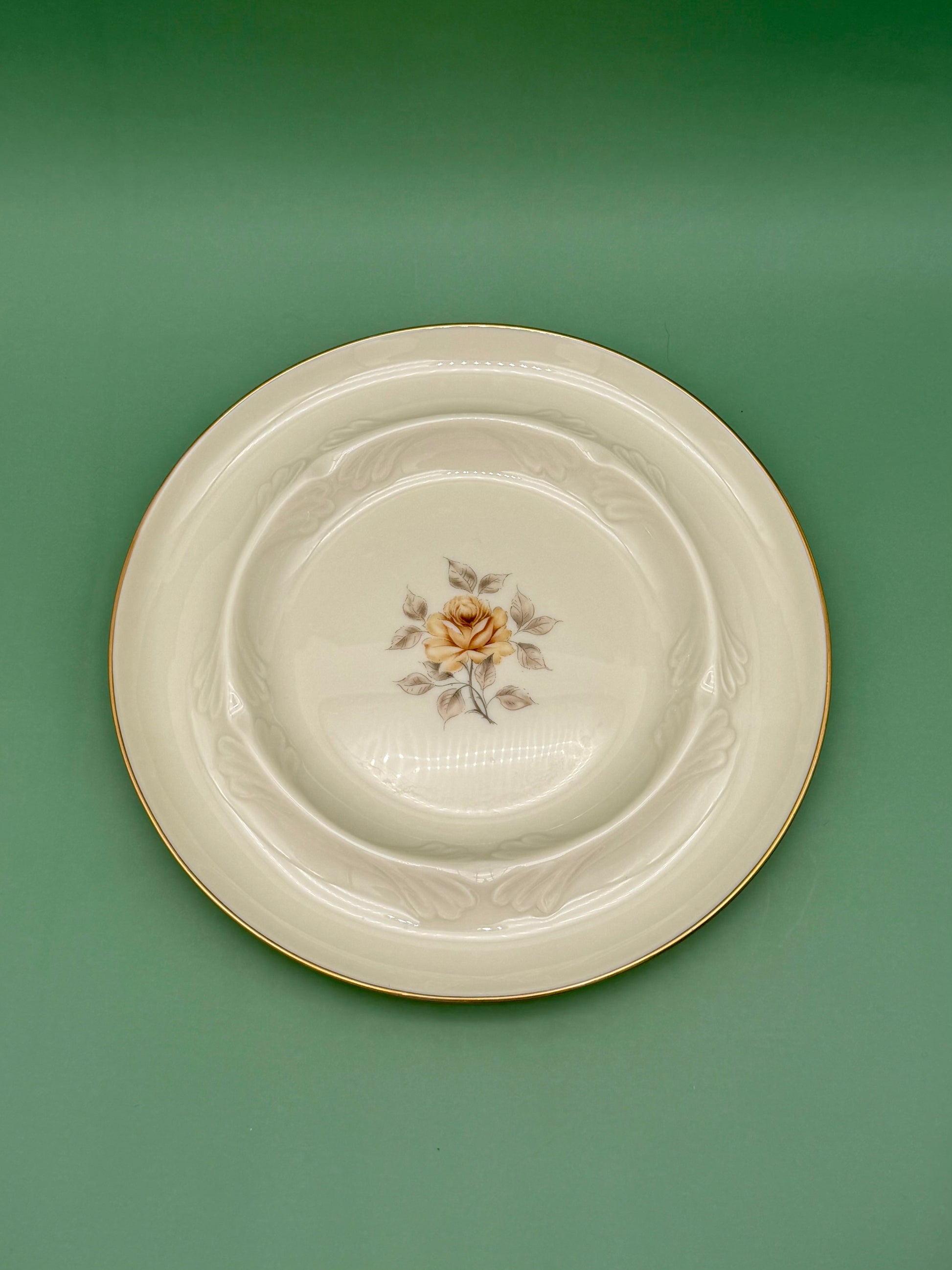 Oval cream ceramic ashtray with a hand-painted pink rose medallion and gold trim, green background.