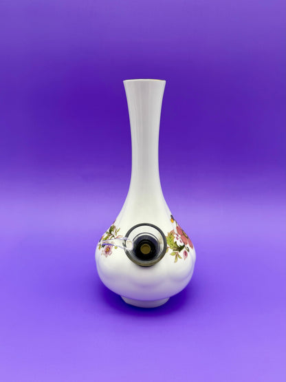 Same white porcelain bud vase water pipe with its floral band, glass bowl piece attached at the front, purple background.