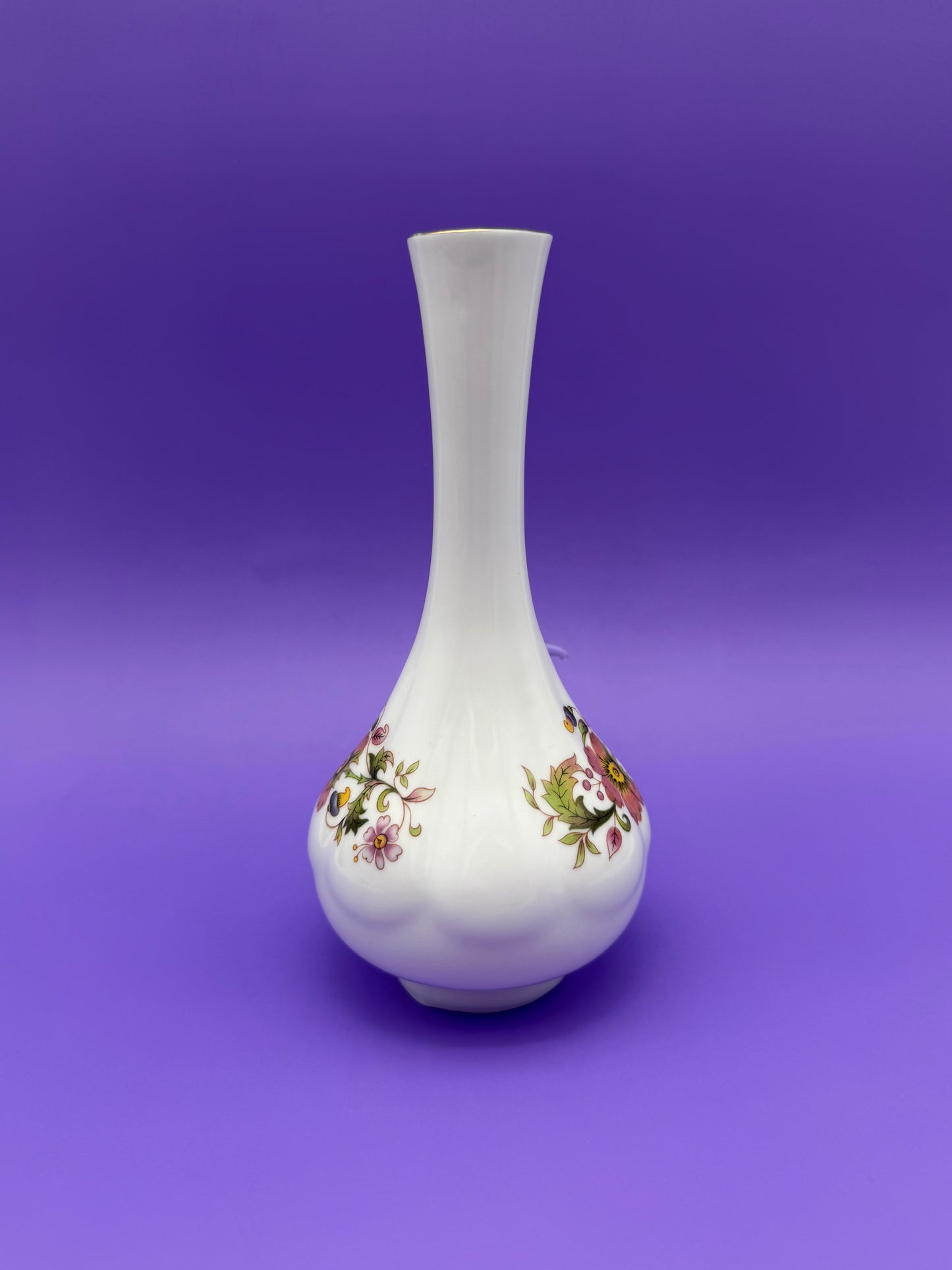 Same white porcelain bud vase water pipe shown without the bowl piece attached, front view of the floral band, purple background.