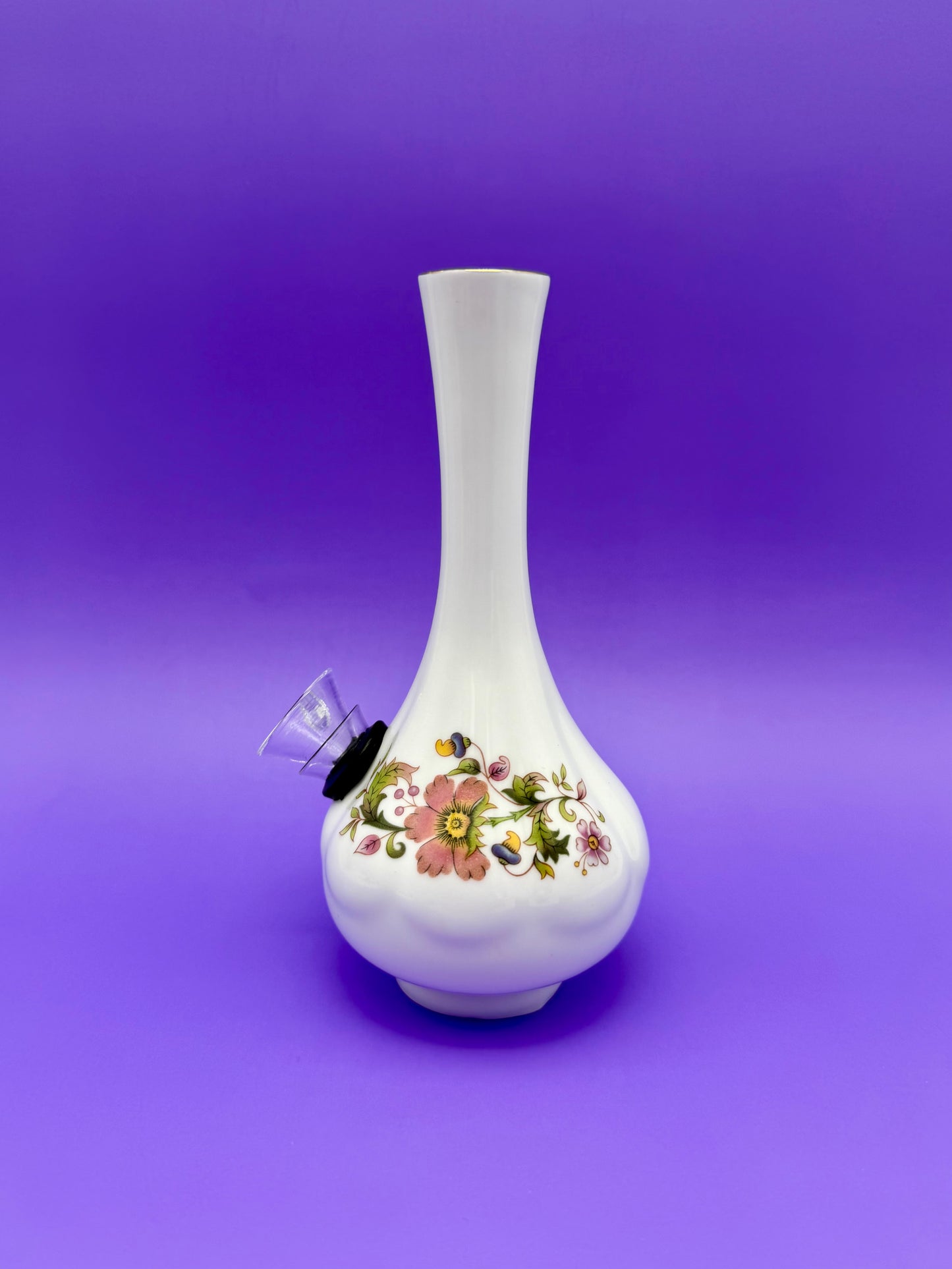 Front view of a white porcelain bud vase water pipe with a floral pattern band, glass bowl piece on the side, purple background.