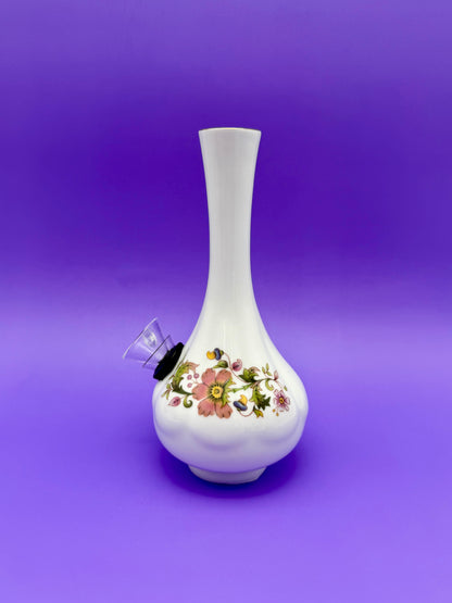 Front view of a white porcelain bud vase water pipe with a floral pattern band, glass bowl piece on the side, purple background.