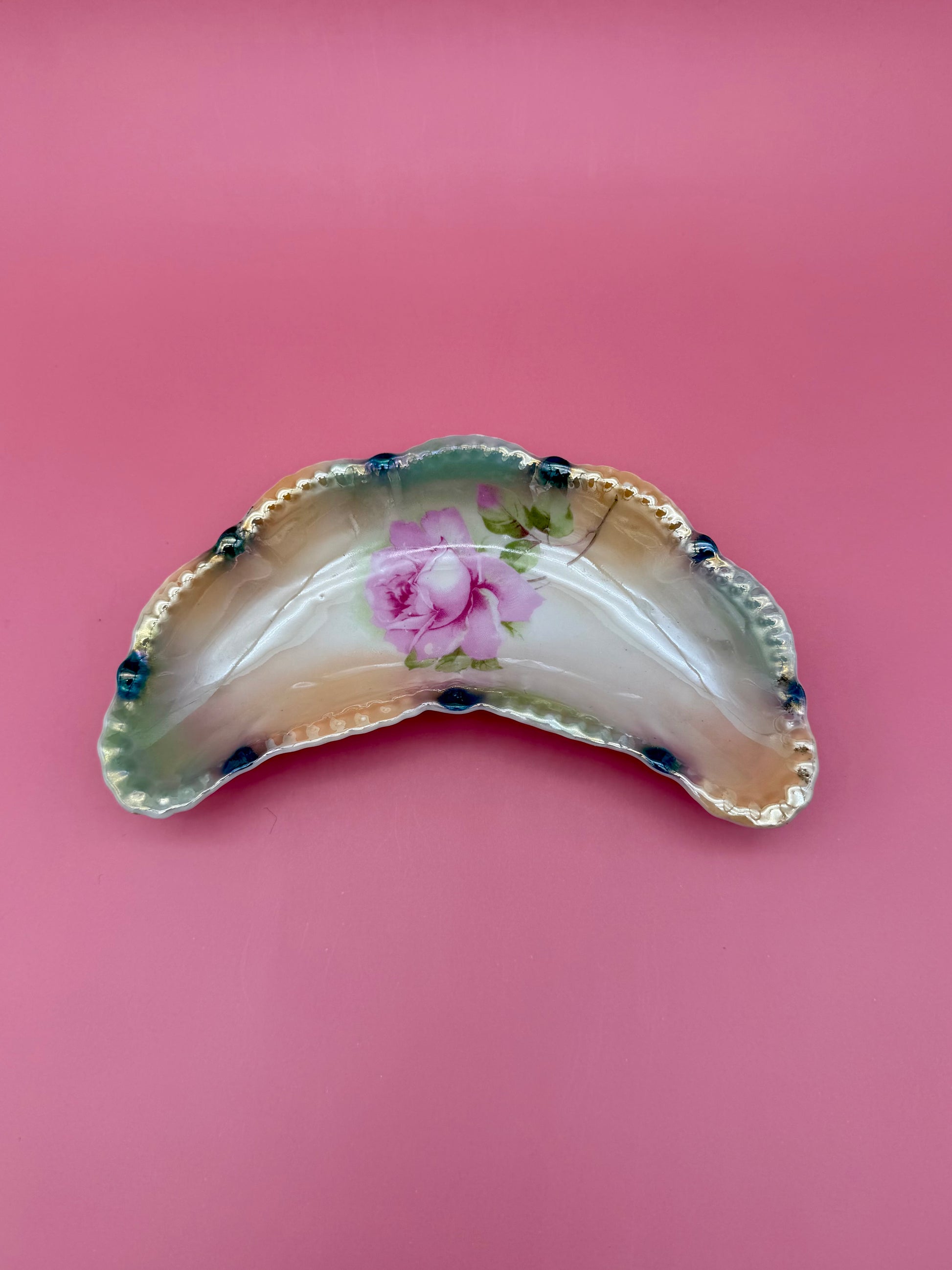 Same crescent-shaped iridescent lustreware ashtray with the hand-painted pink rose design, shown without the cigarette pick, closer view, pink background.
