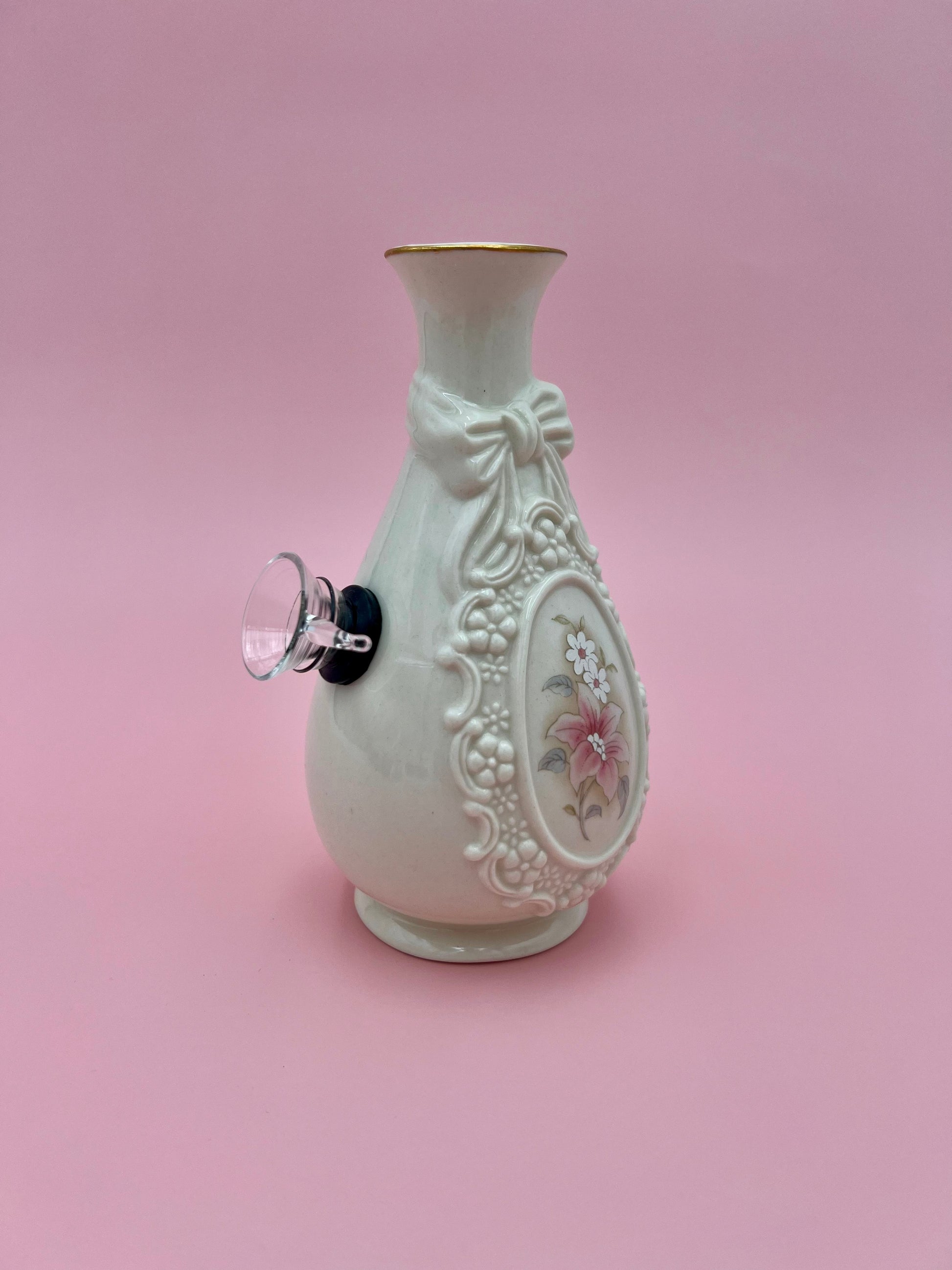 Three-quarter view of the same cream Louise water pipe showing the embossed bow detail and glass bowl piece, pink background.