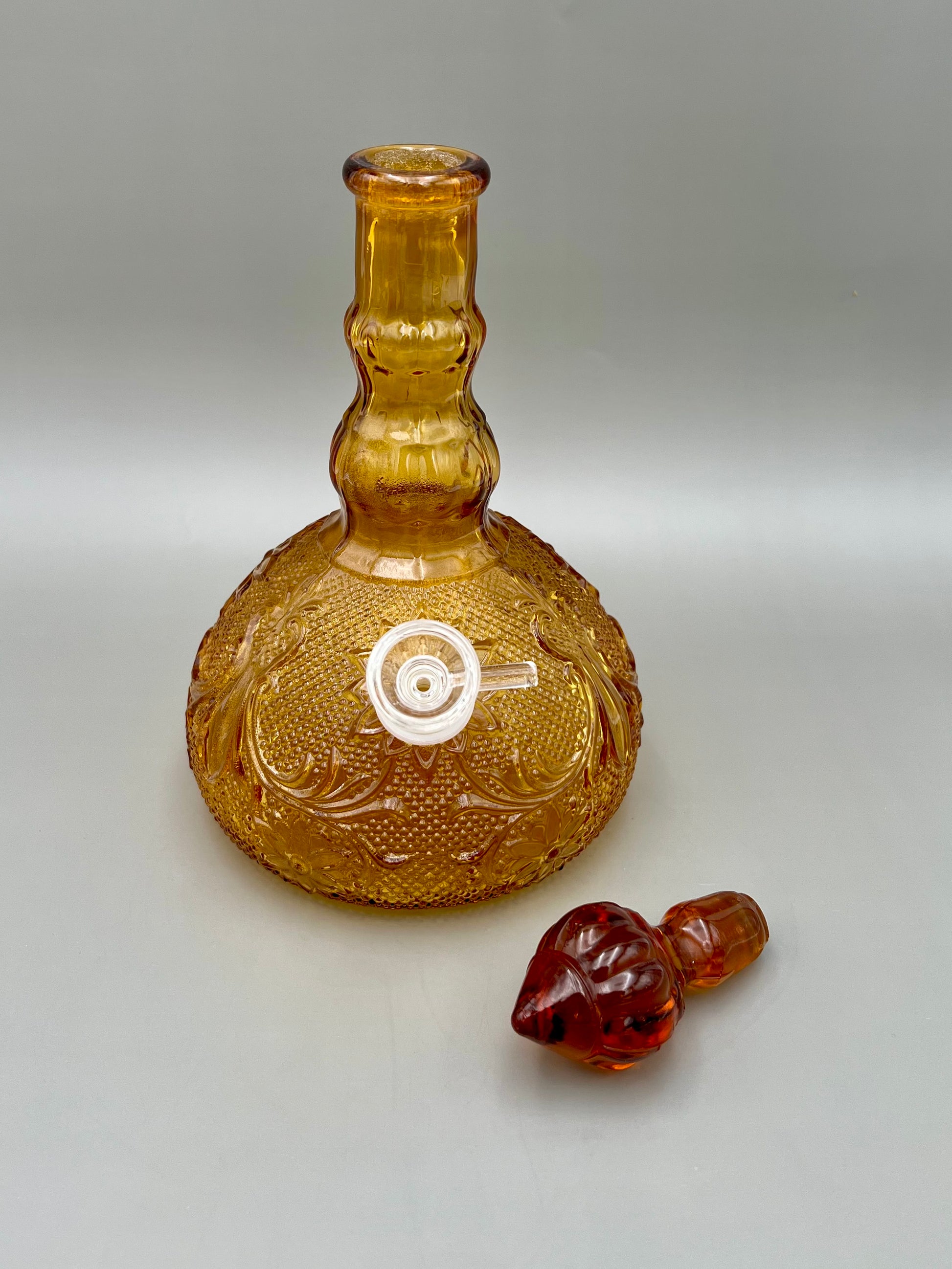 Same amber pressed-glass decanter with the stopper removed and set beside the base, showing the open neck, gray background