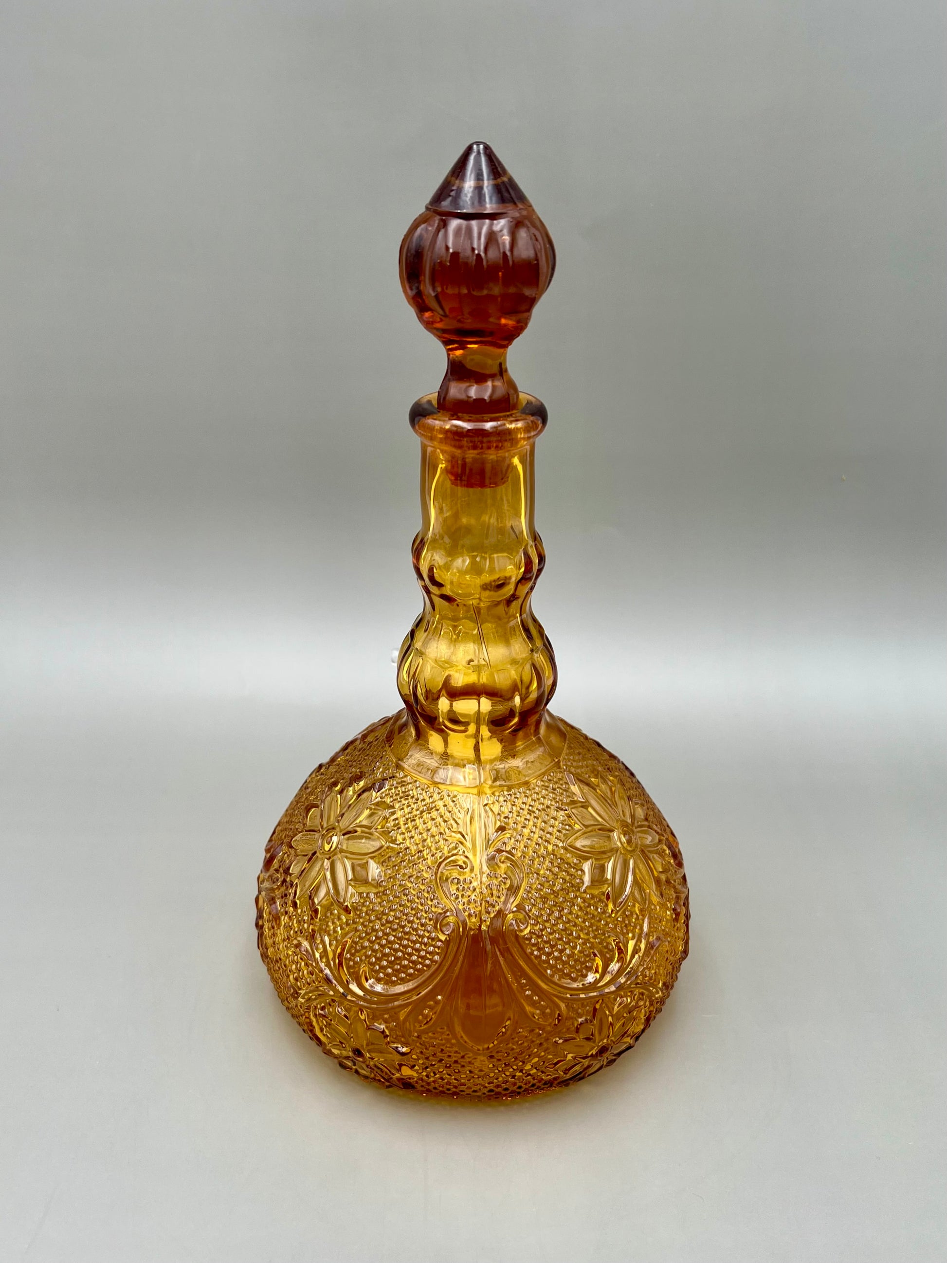 Same amber pressed-glass decanter in a plain front view with stopper in place and no attachment visible, gray background