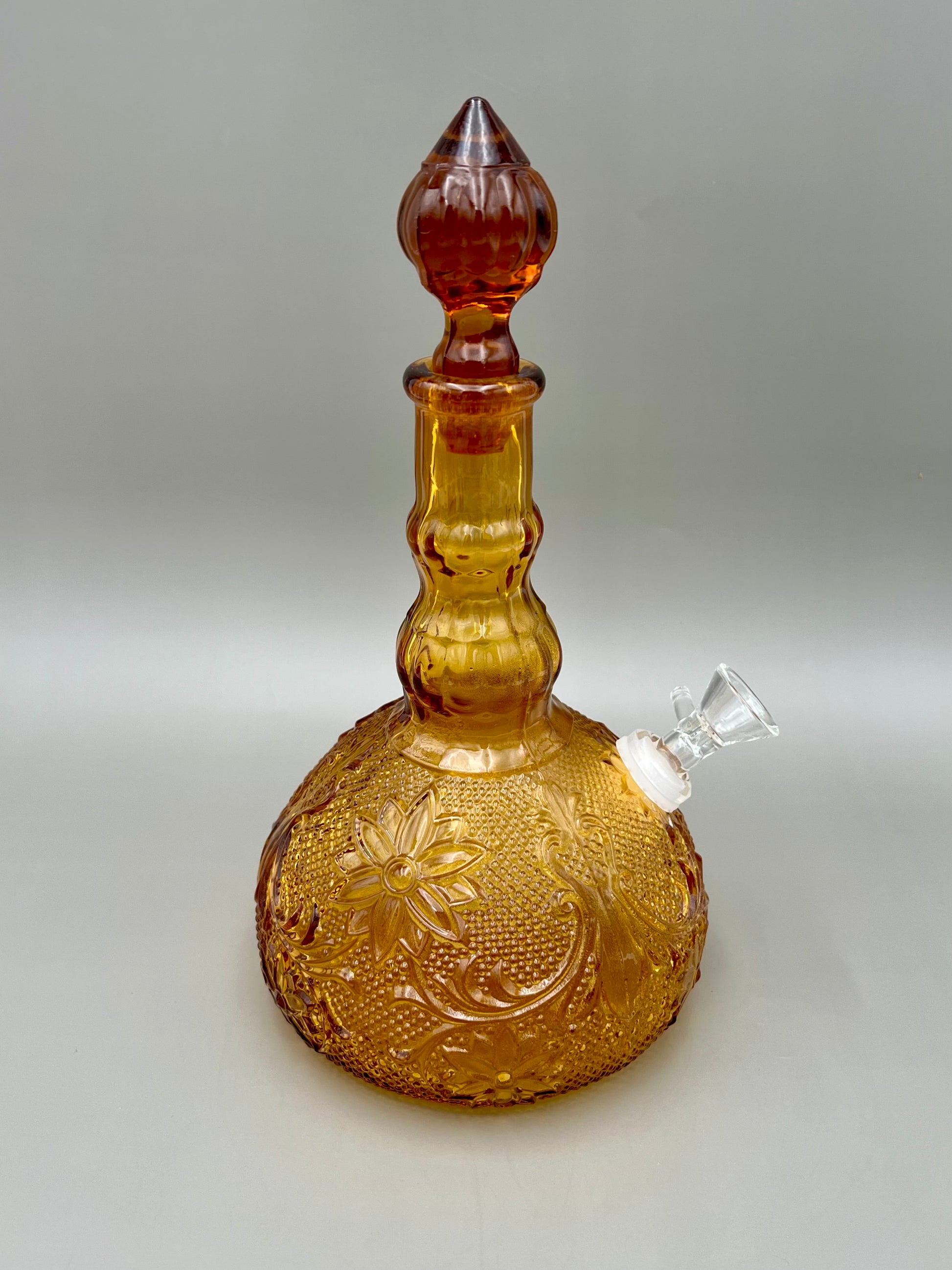 Same amber pressed-glass decanter viewed at a slight angle with a clear glass mouthpiece attached near the neck, gray background