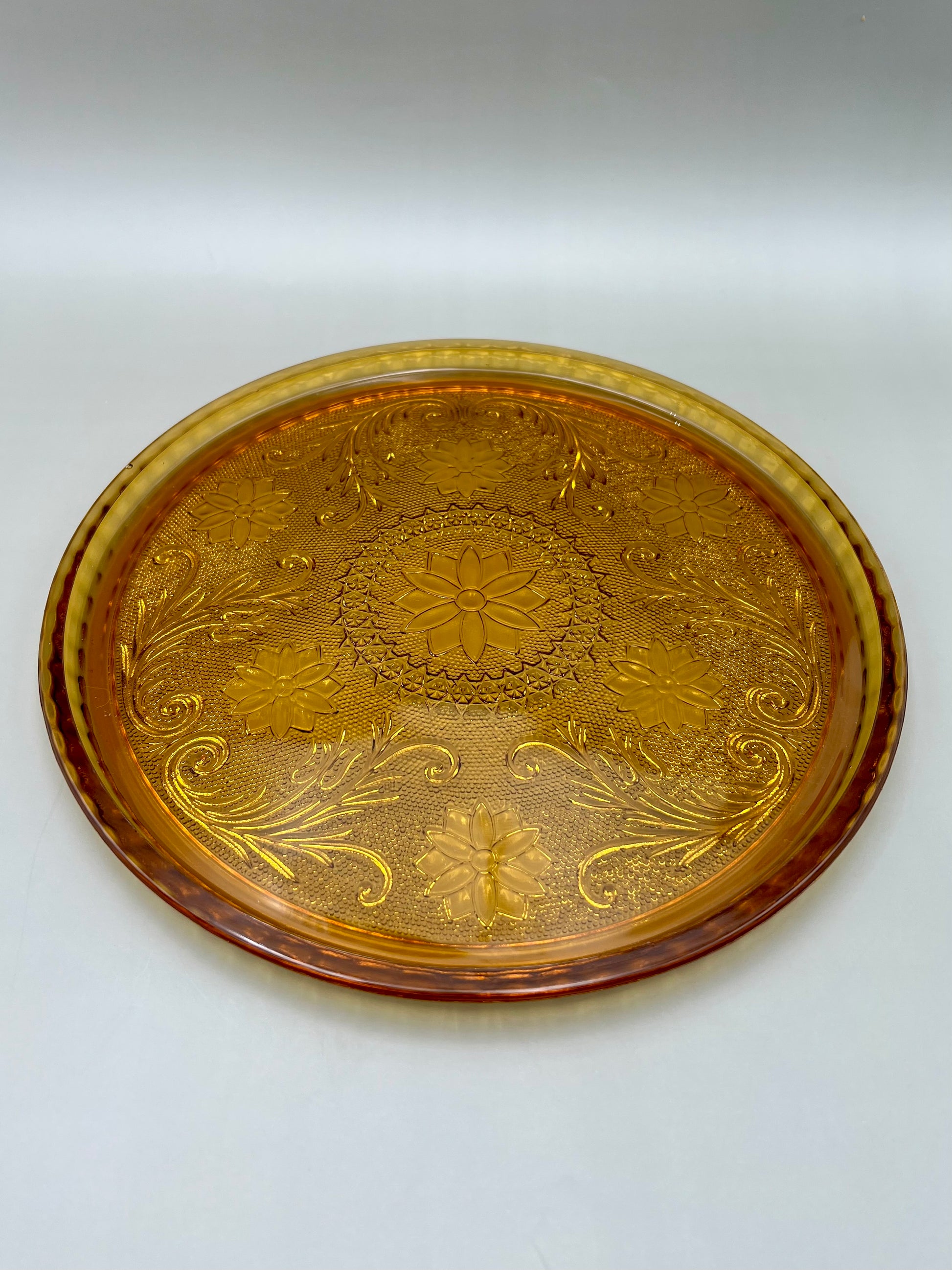 Round amber pressed-glass serving tray with a matching embossed baroque pattern, gray background
