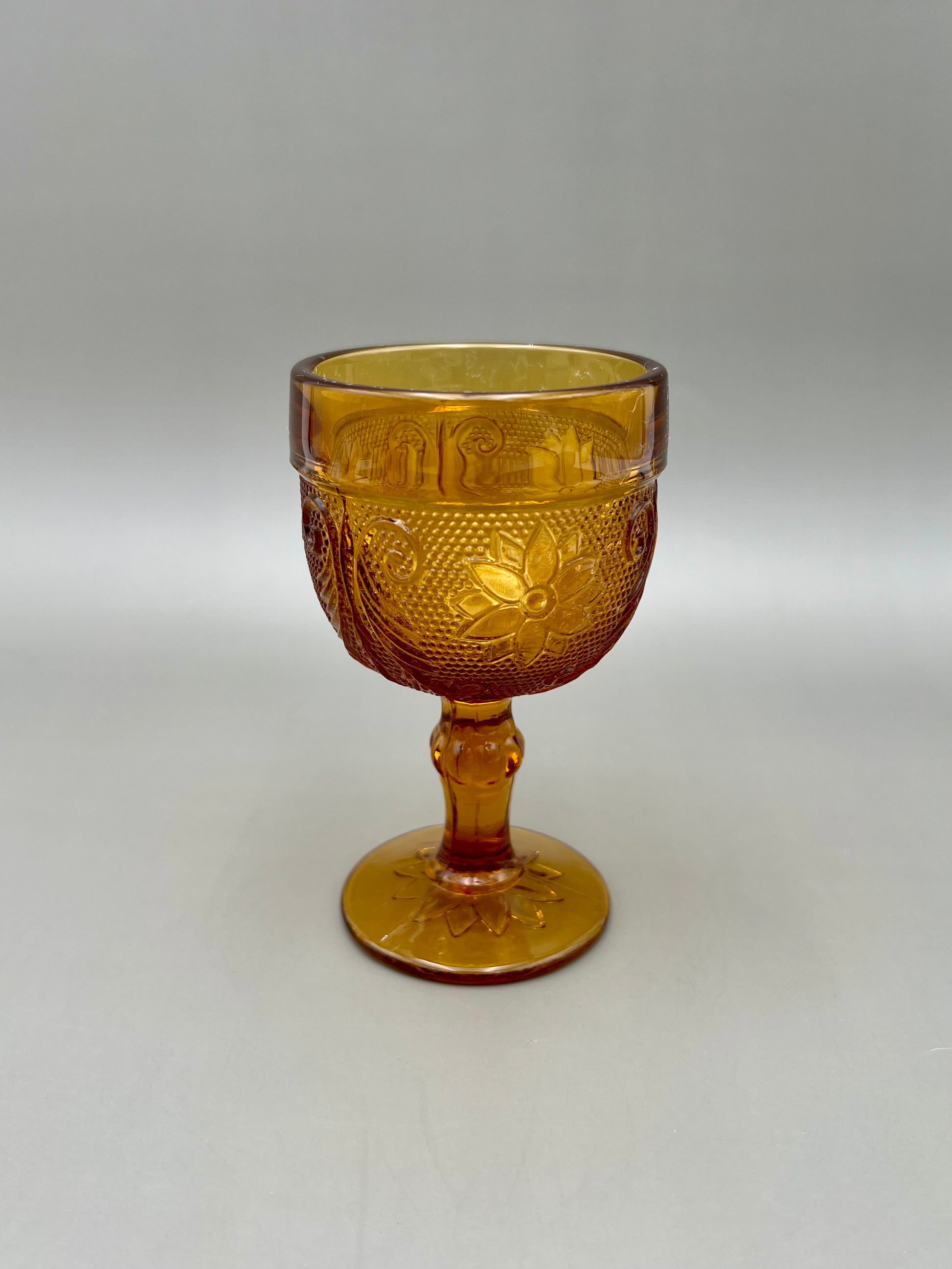 Single amber pressed-glass cordial goblet shown alone, gray background