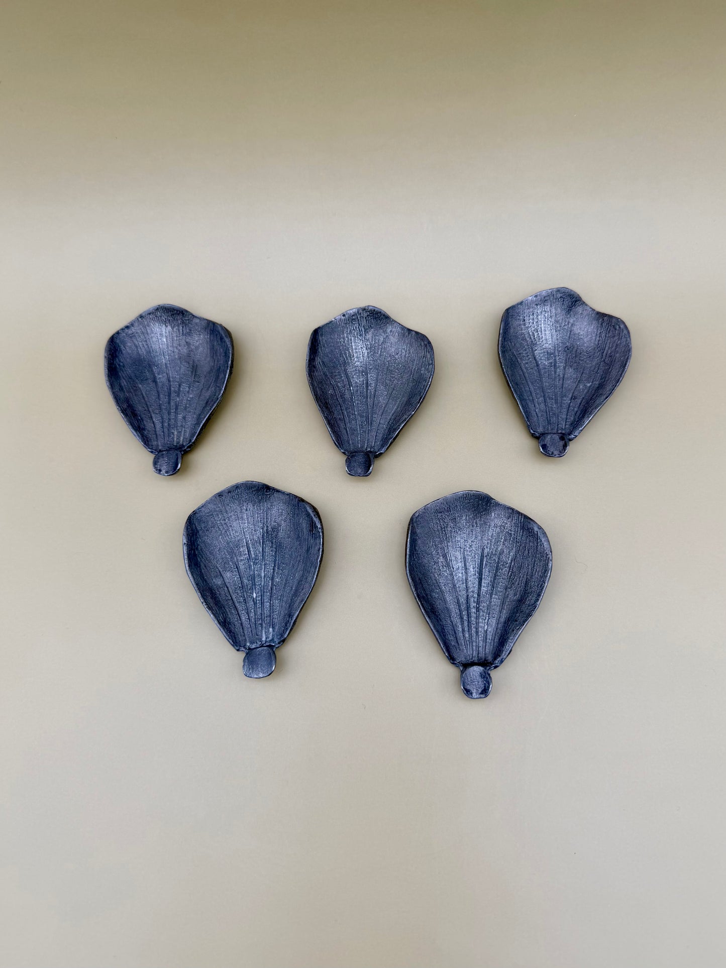 Five silver teardrop-shaped petal dishes scattered separately, tan background.