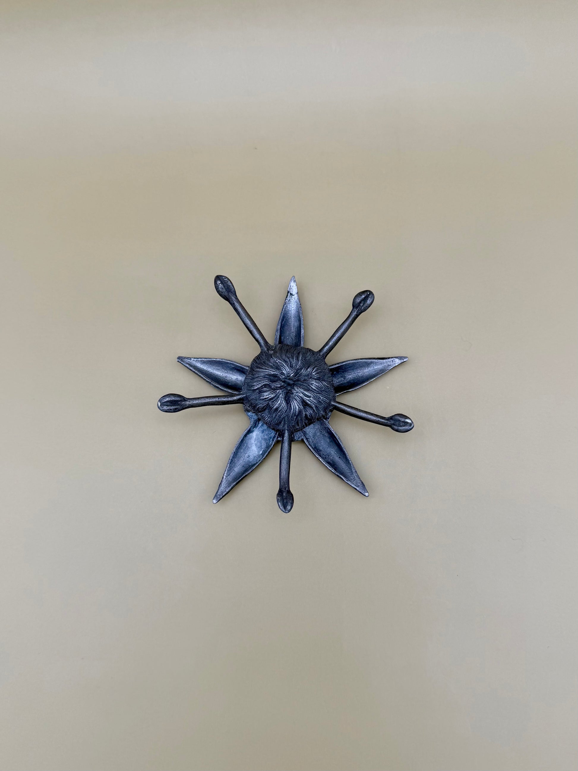 Silver starburst-shaped dish with pointed rays radiating from a textured center, tan background.