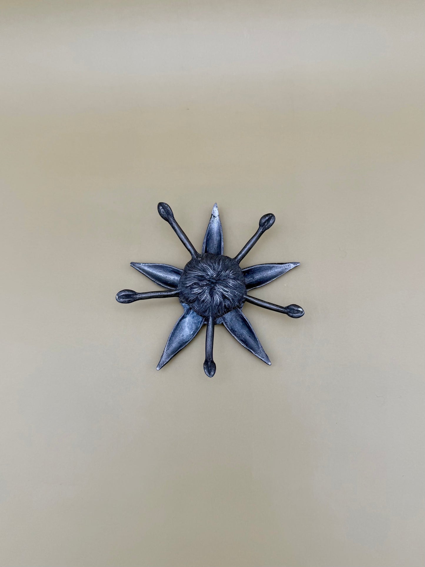 Silver starburst-shaped dish with pointed rays radiating from a textured center, tan background.