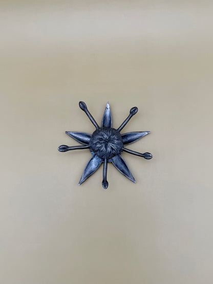 Silver starburst-shaped dish with pointed rays radiating from a textured center, tan background.
