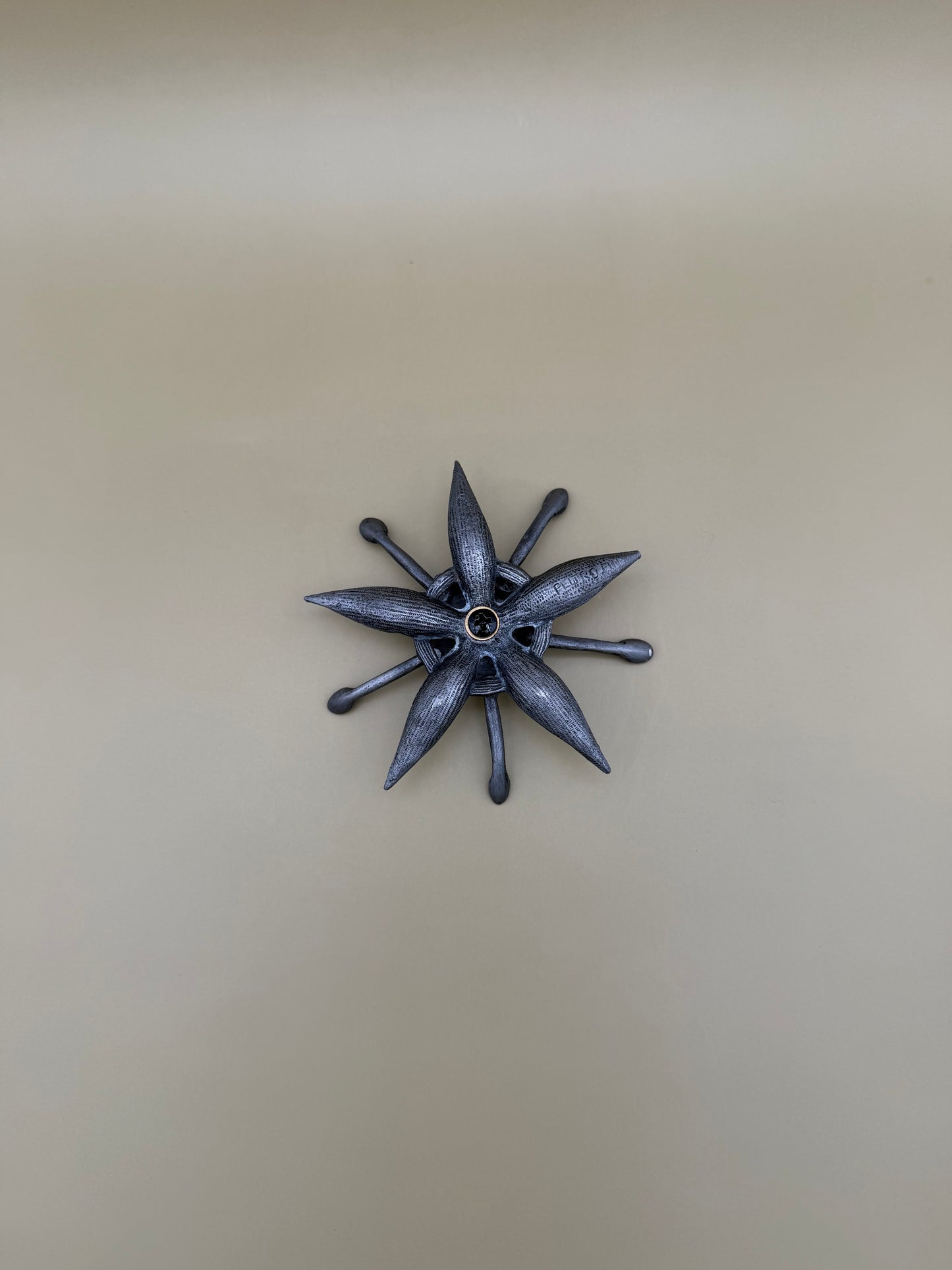 Similar silver starburst-shaped dish with pointed rays and a small round center accent, tan background.