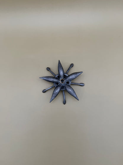 Similar silver starburst-shaped dish with pointed rays and a small round center accent, tan background.