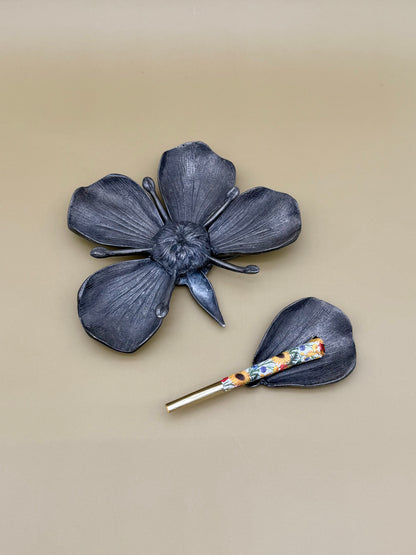 Silver marigold flower-shaped dish with five petals, paired with a small teardrop-shaped petal dish holding a floral-patterned glass cigarette pick, tan background.