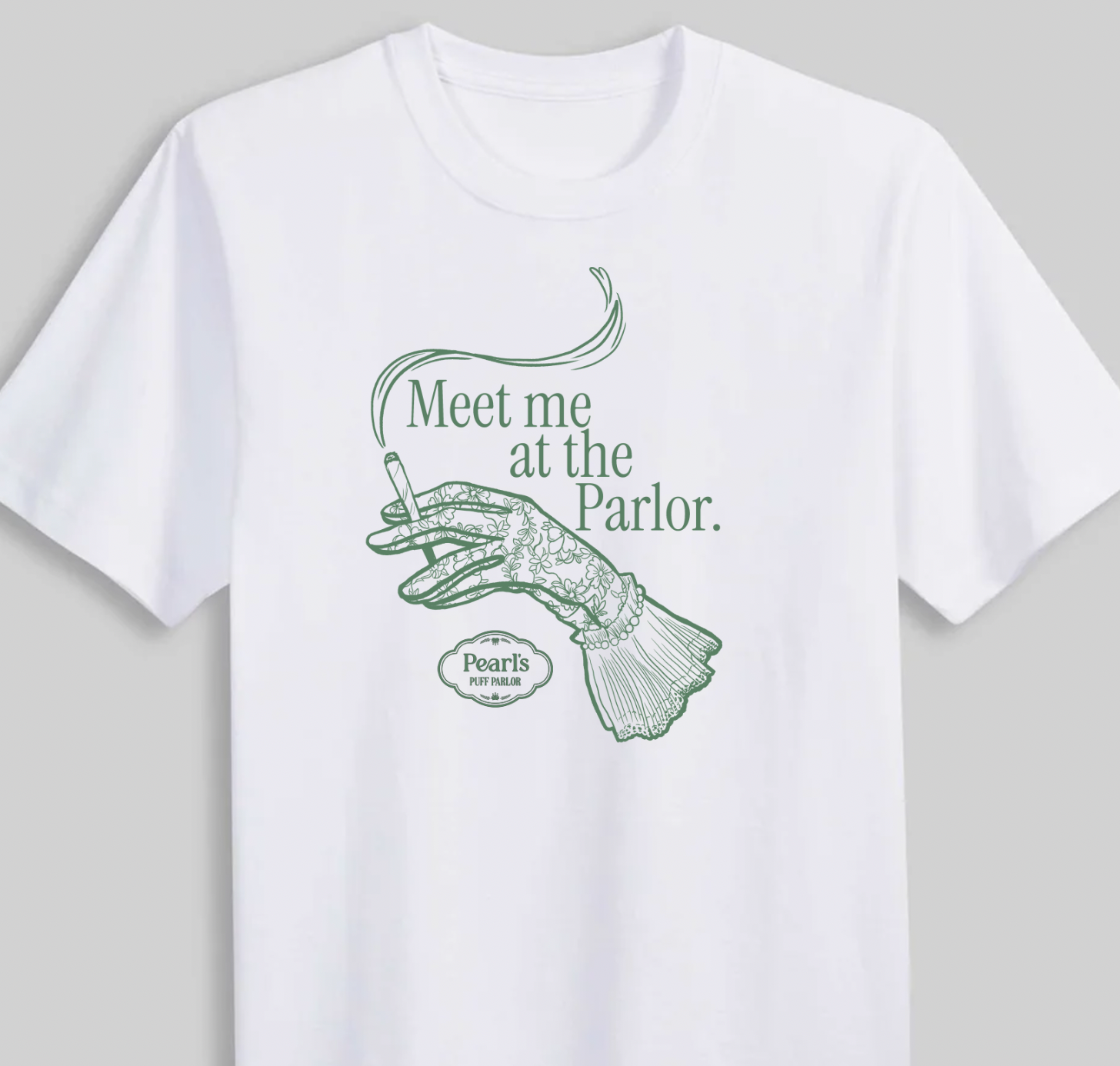 White t-shirt printed with a simple line-art illustration of a gloved hand holding a cigarette and the text 'Meet me at the Parlor,' with a small logo below, flat lay on a gray background.