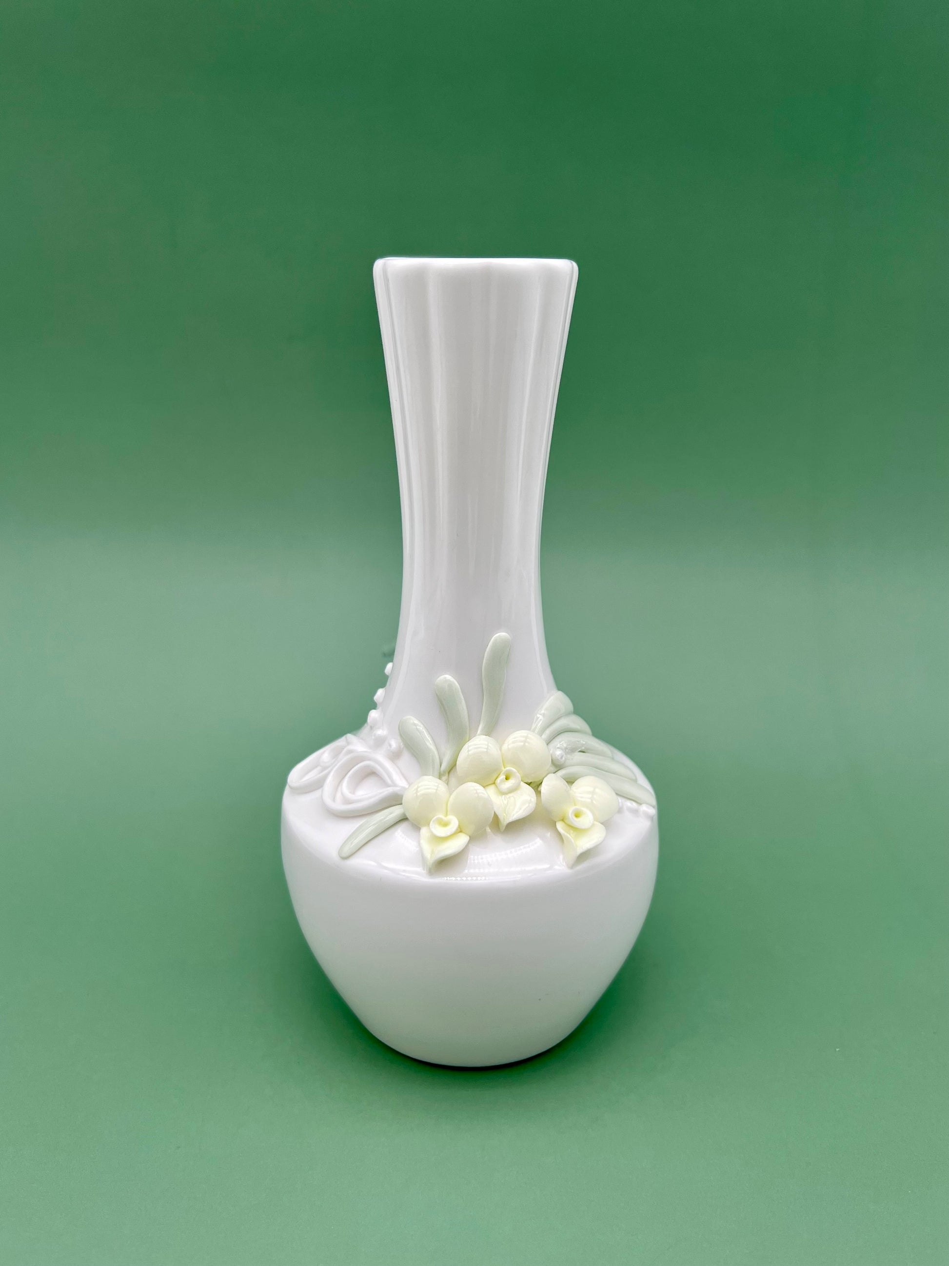 Front view of a tall white porcelain bud vase water pipe with sculpted white flowers at the base, green background.