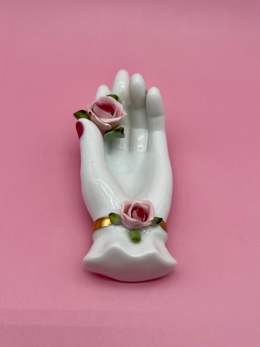 White porcelain ashtray shaped like an elegant hand adorned with pink roses at the wrist, pink background.